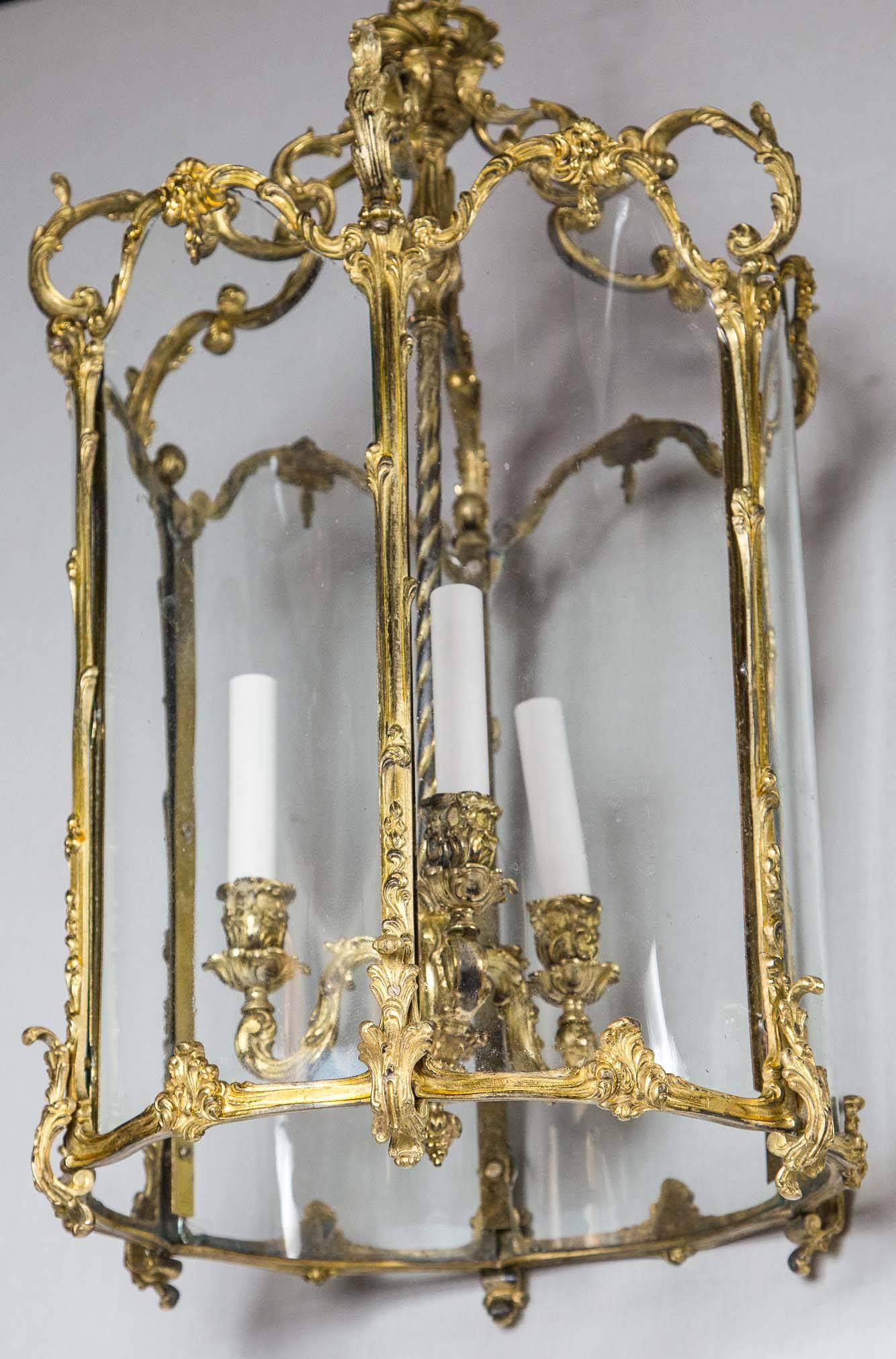 Solid gilt bronze six sided cage with three suspended electrified candle cups in the Louis XV Rococco manner with foliates and scrolls. Six glass panels. The height of 26 inches does not include any chain.