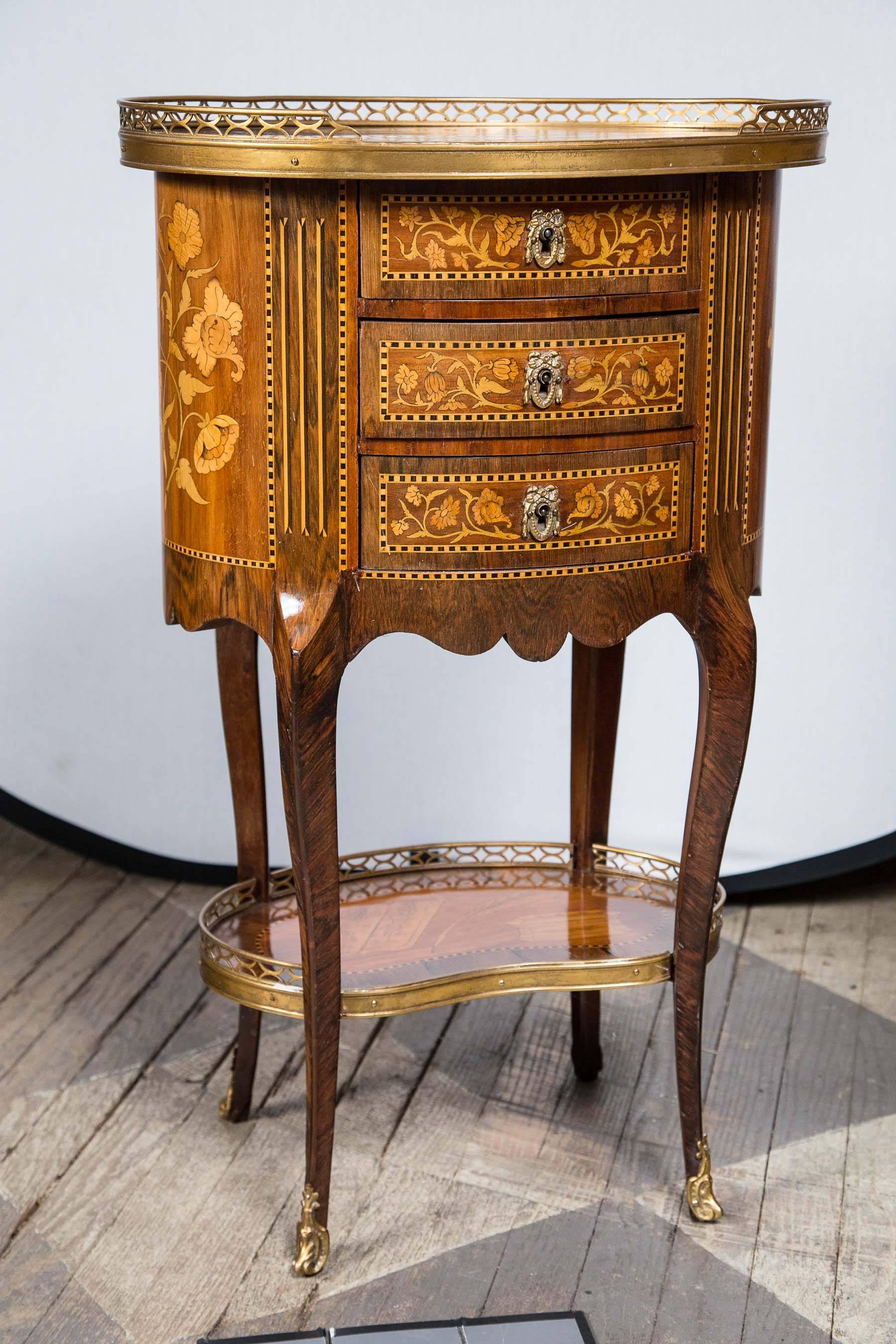 In the Louis XV style, these are in refinished condition. Each has a 3/4 brass gallery on the top and lower shelf with brass edging. Brass sabot on the feet. Three drawers, the top of one shows marquetry of flowers and leaves, while the other has a