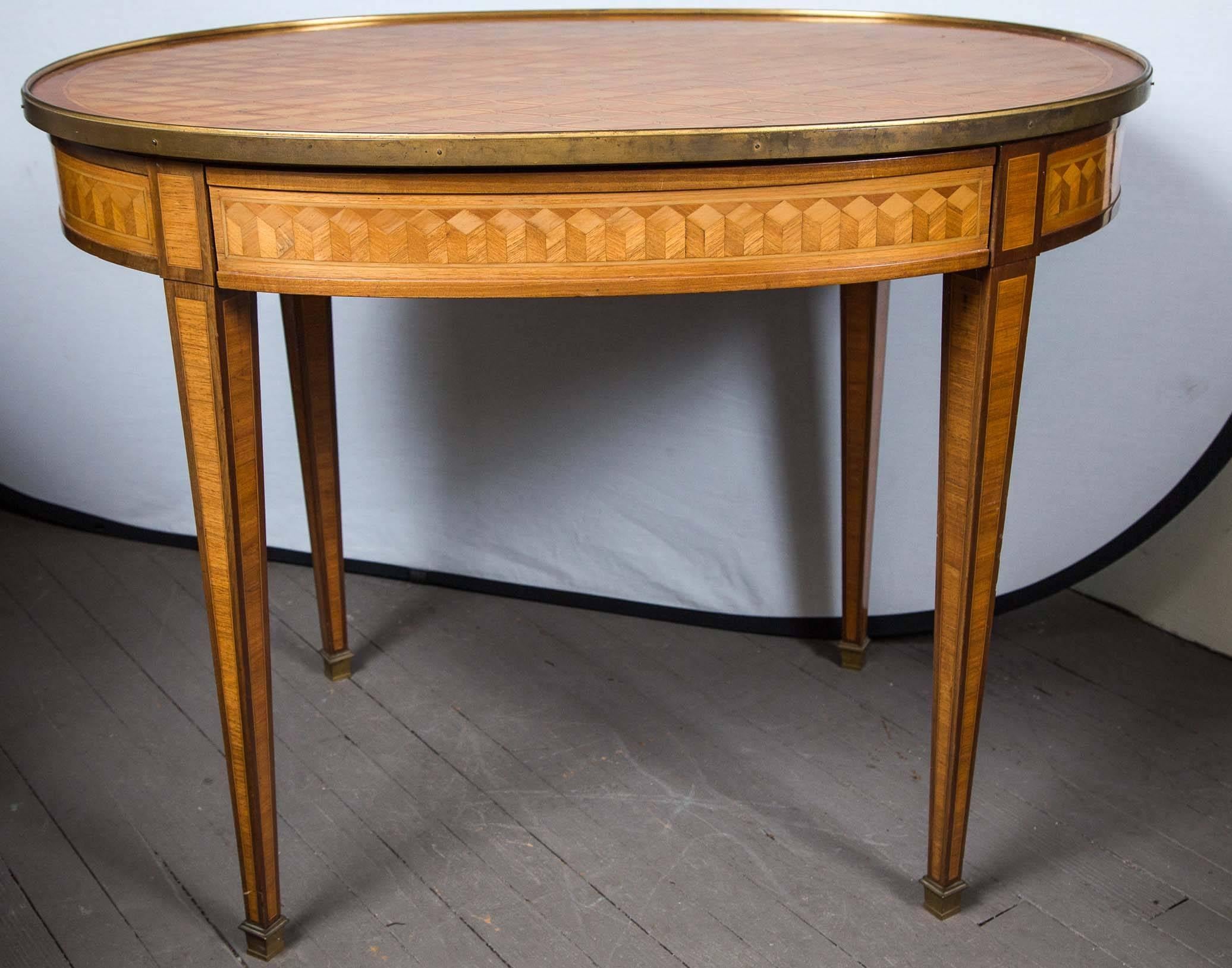 The oval brass edged top of cross hatched parquetry, the apron of tromp l'oeil marquetry. A single drawer in the apron.
Raised on squared tapered legs ending in brass sabot caps.