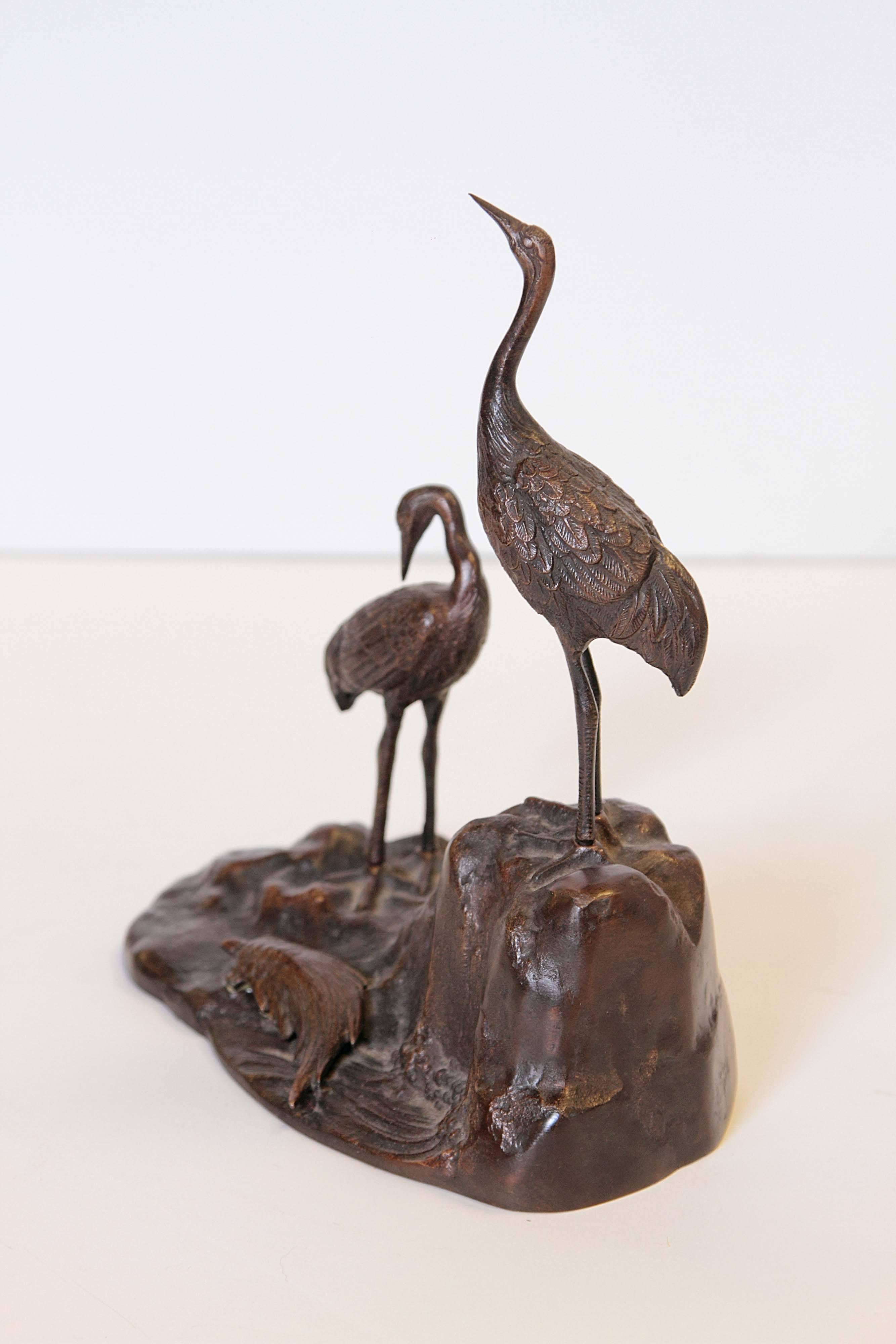 Bronze sculpture of Japanese cranes on a rocky shoreline. A small mminogame, a Japanese mythological long-tailed turtle, is also depicted emerging from the surf onto the rocks.