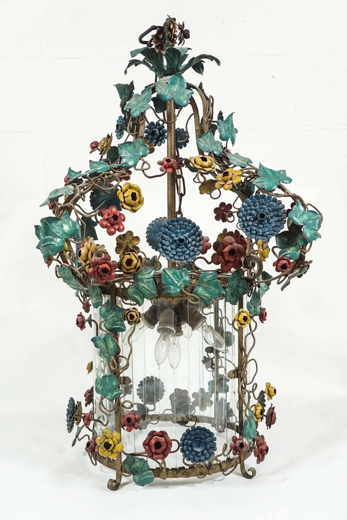 Here is a beautiful French polychrome tole flower chandelier with a large glass cylinder insert. There is an ivy motif throughout that climbs to the top. There are five light sockets inside.