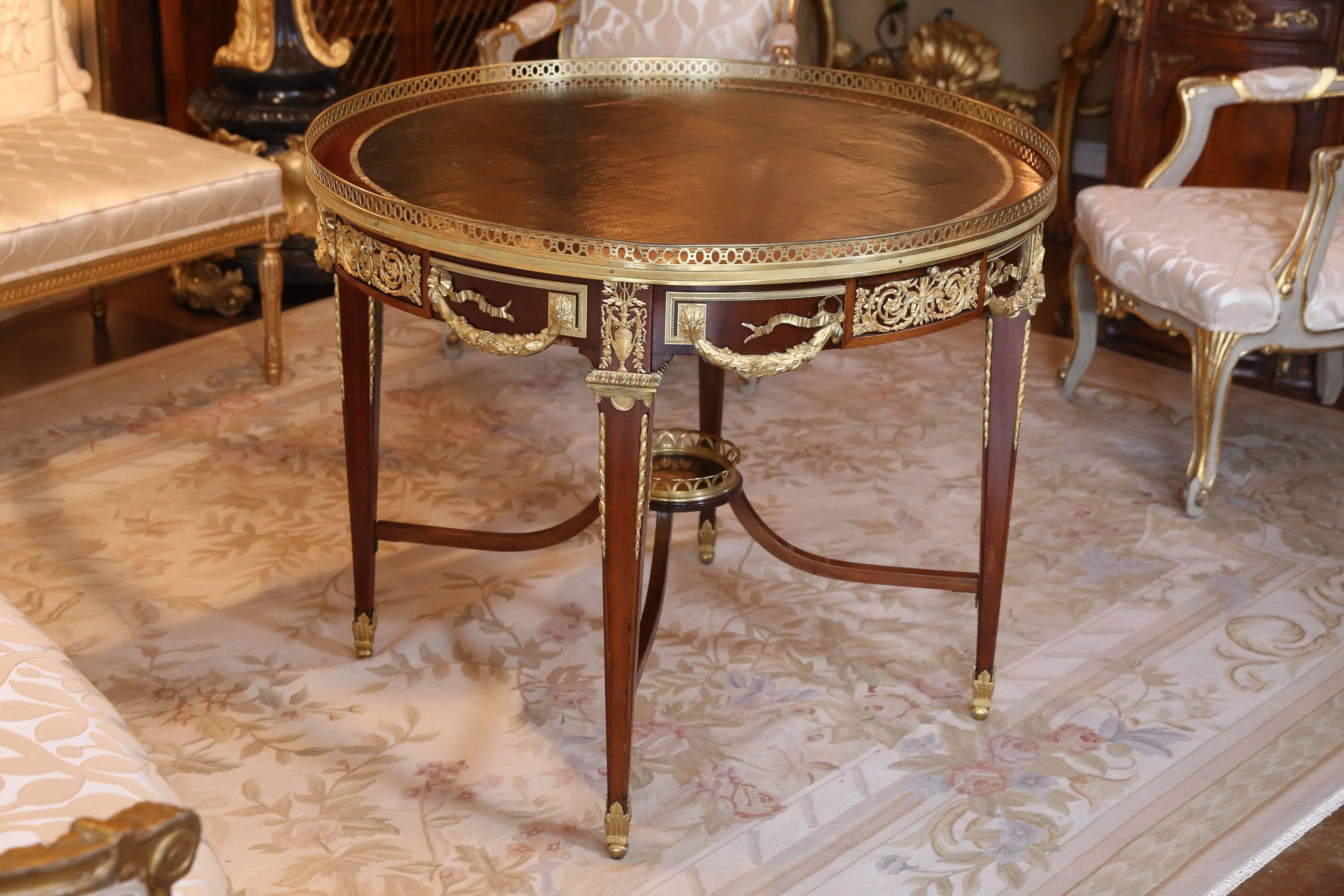 Round French center table with brass gallery, two-drawers and four sides in the apron, the whole decorated with elaborate gilt bronze mounts, standing on 
four square tapered legs with ormolu feet and connected by upswept stretchers with central