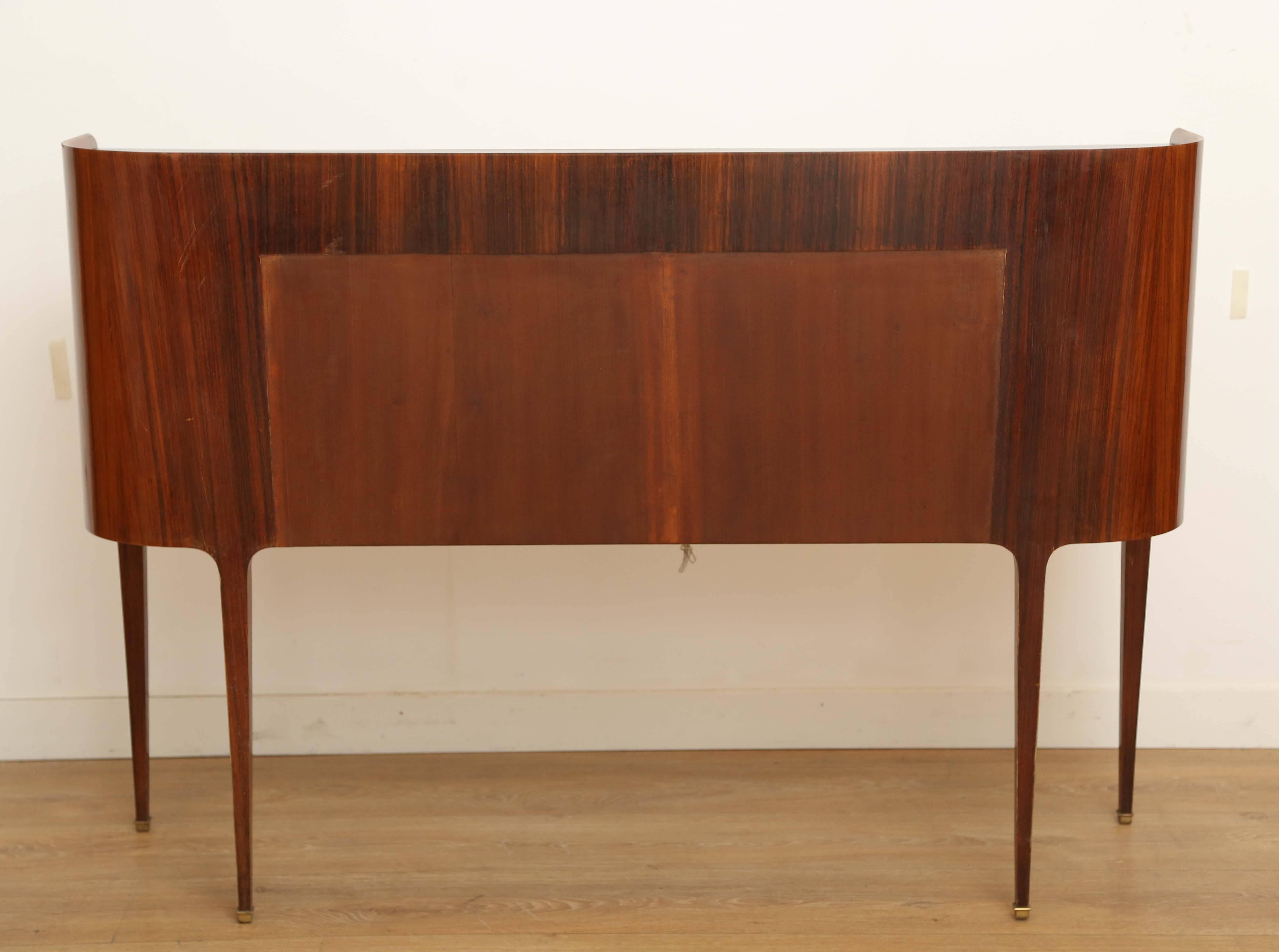 Rare mid-century modern dry bar cabinet by Paool Buffa. Graciously curved Indian rosewood encasement with a drop down front open to a full-service bar with plenty of room. Tapered legs with bronze sabots. Burgundy inset glass top. Maple interior