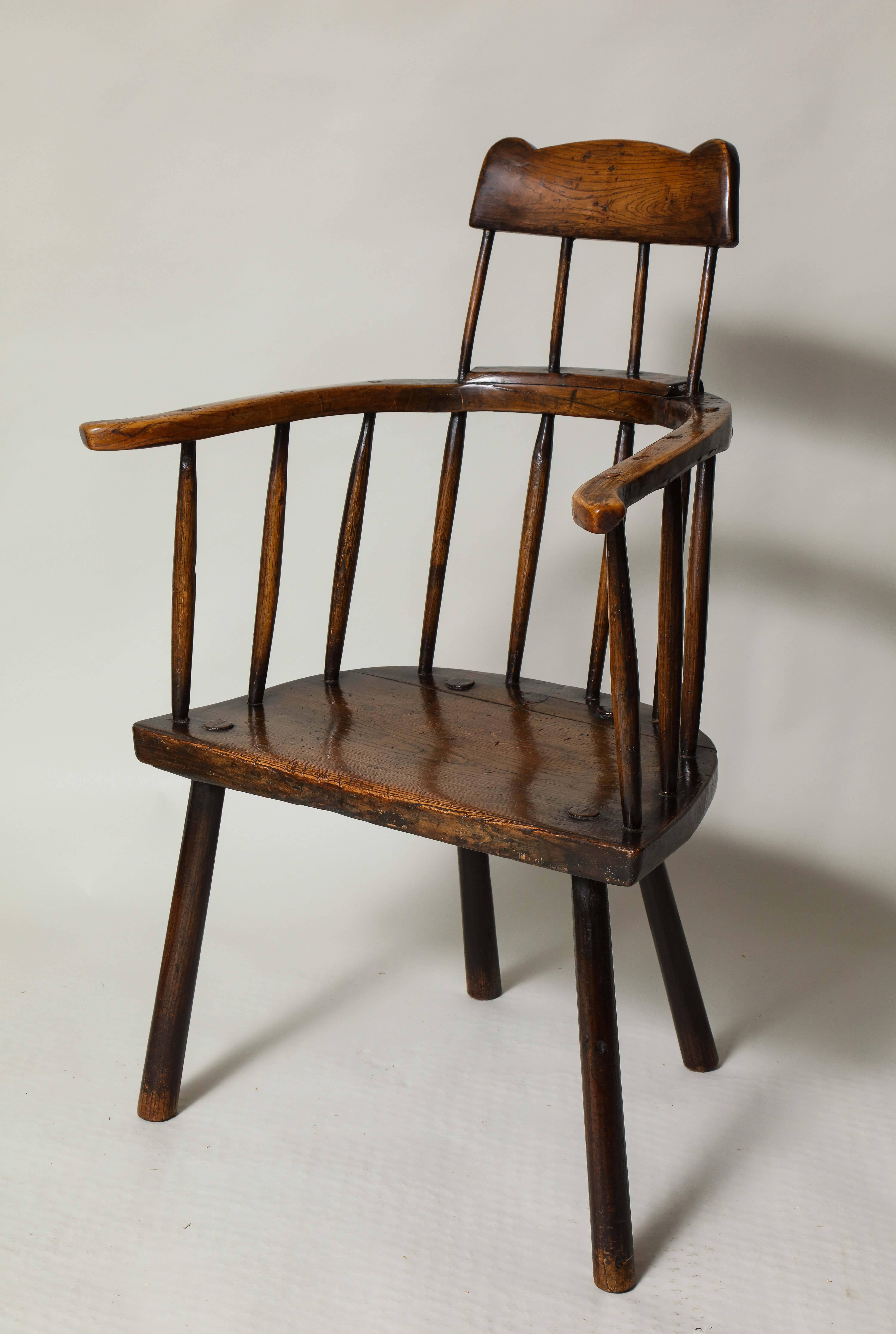 A unique primitive windsor chair with curved and eared comb-back crest rail over outs wept arm bow with slab elm seat standing on stick legs. Rich patination. A sculptural and whimsical folk piece. Welsh, 18th century.
