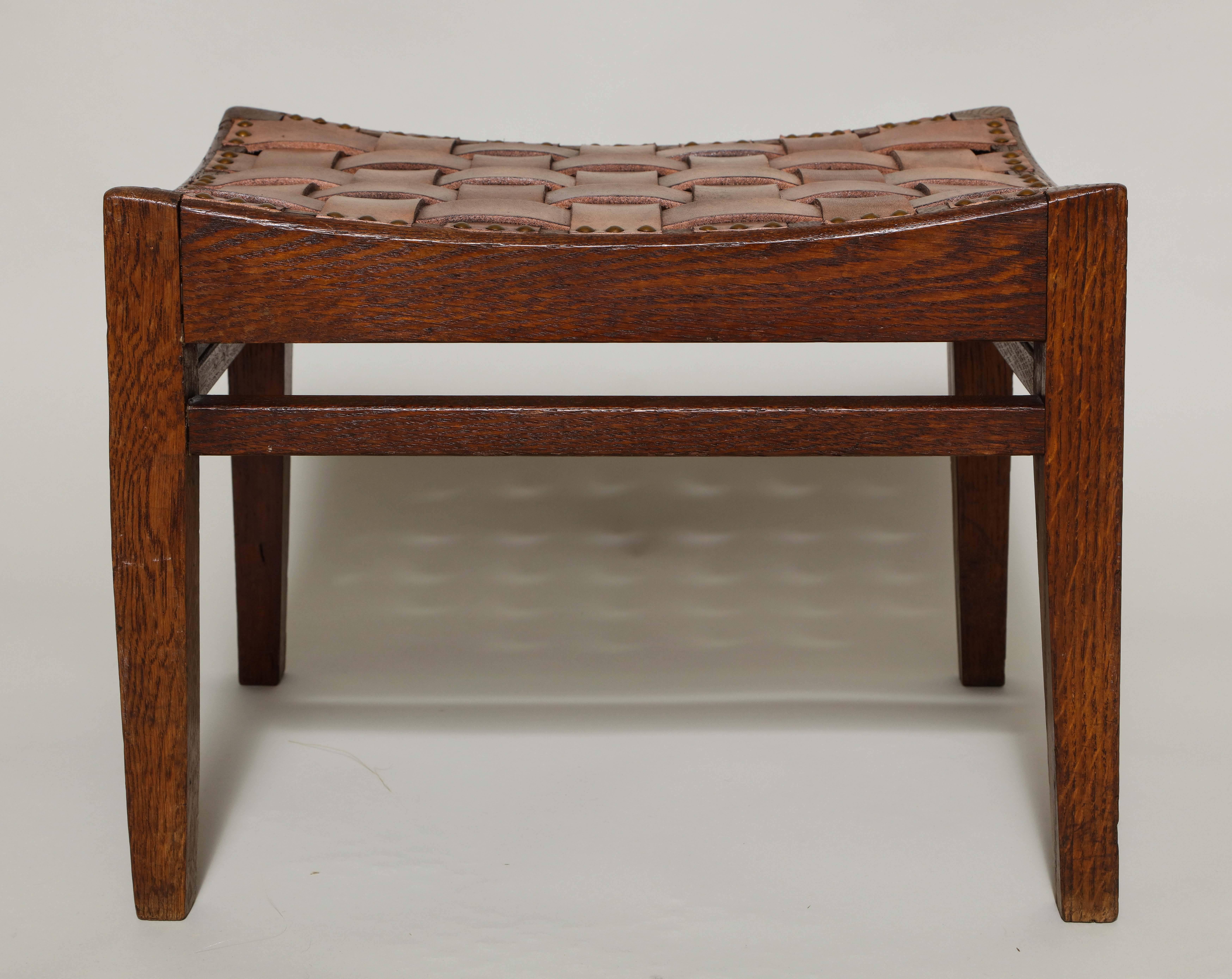 Good English Arts & Crafts period stool by Arthur Simpson of Kendal, having woven leather strap work with studs, on dished seat rails, the four legs joined by high box stretcher.