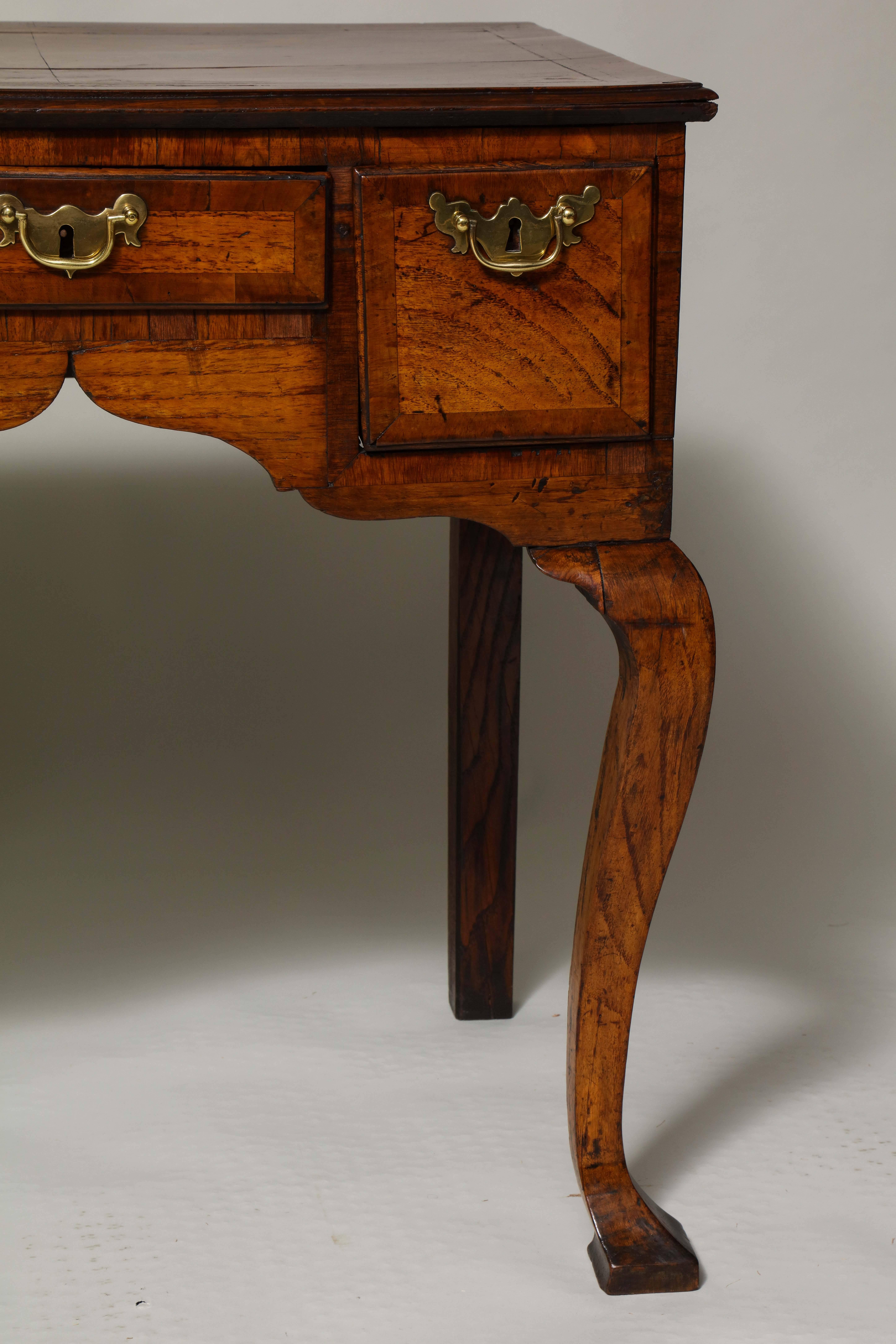 Early 18th century English oak and walnut lowboy, the quarter bookmatched top with herringbone stringing and walnut crossbanding, over two deep and one shallow drawer with crossbanded edges, standing on square shaped legs with suggestions of a