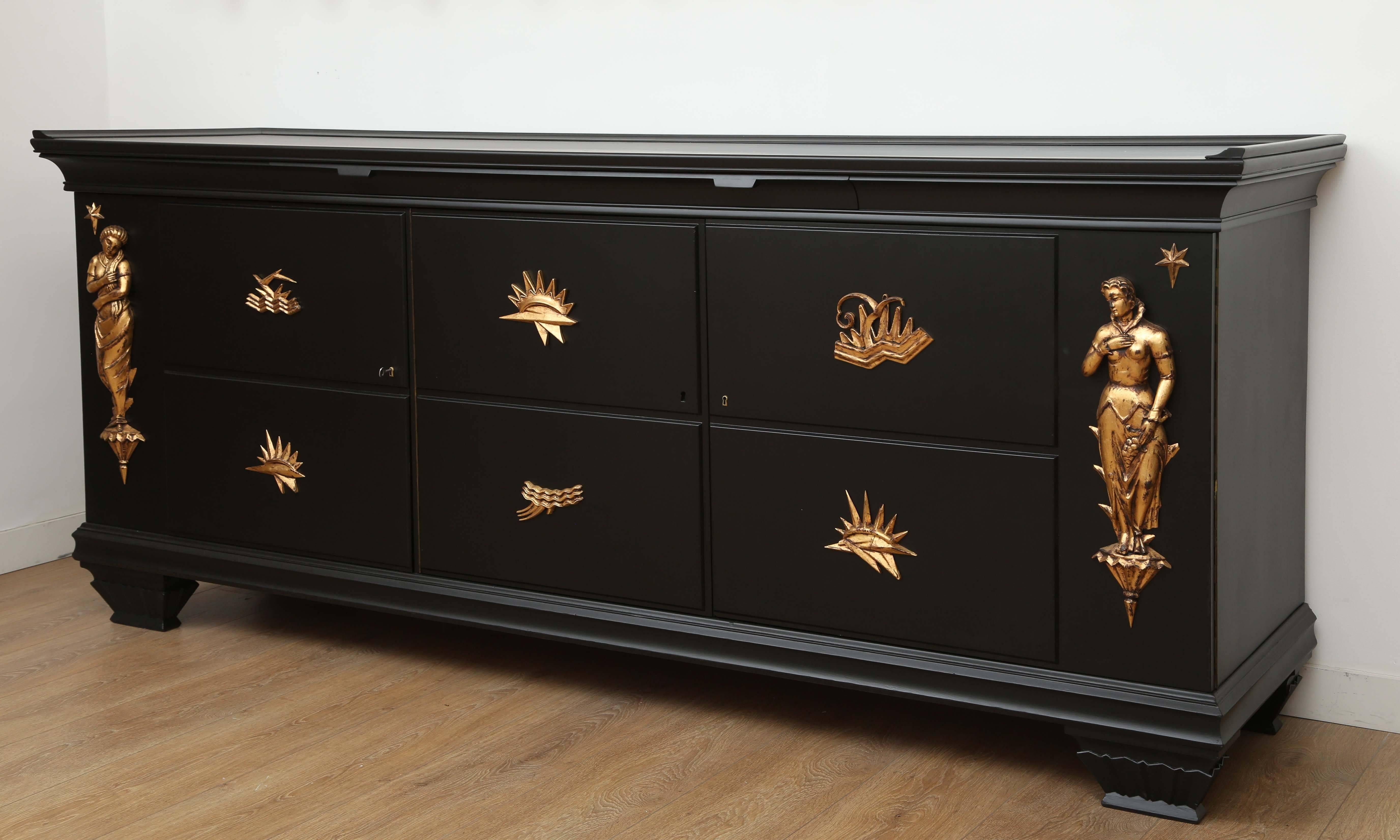 A large black lacquered three-door sideboard with giltwood cariatides at either end, each door is divided into two panels with an applied carved giltwood abstract element. Cabinet has a pullout service surface just beneath the top at the centre.