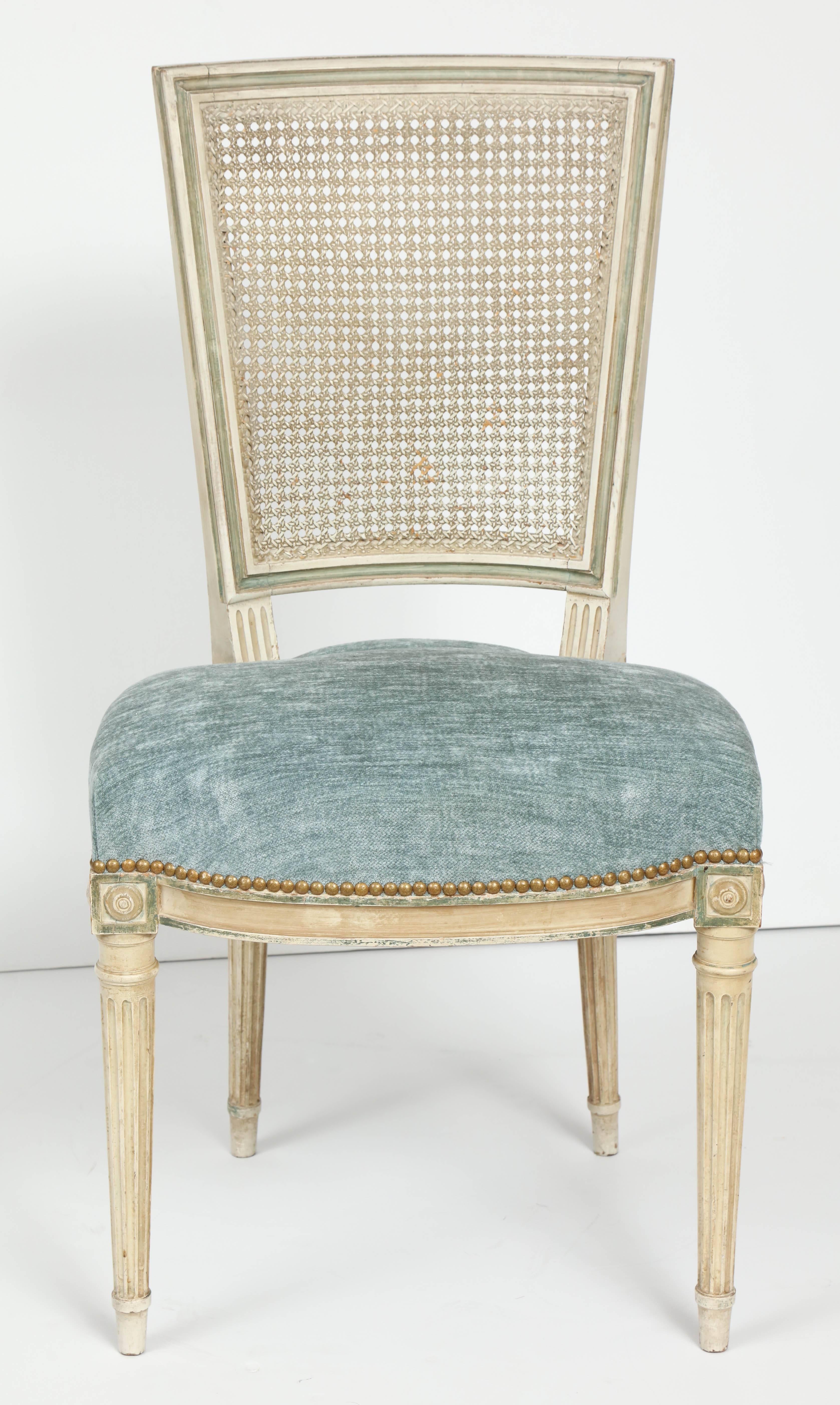 A set of refined and striking Louis XVI style dining chairs. These beautiful chairs are painted is a soft, creamy white with blue/gray accents. The squared back is caned and the slightly rounded seat is upholstered in a pale blue chenille with