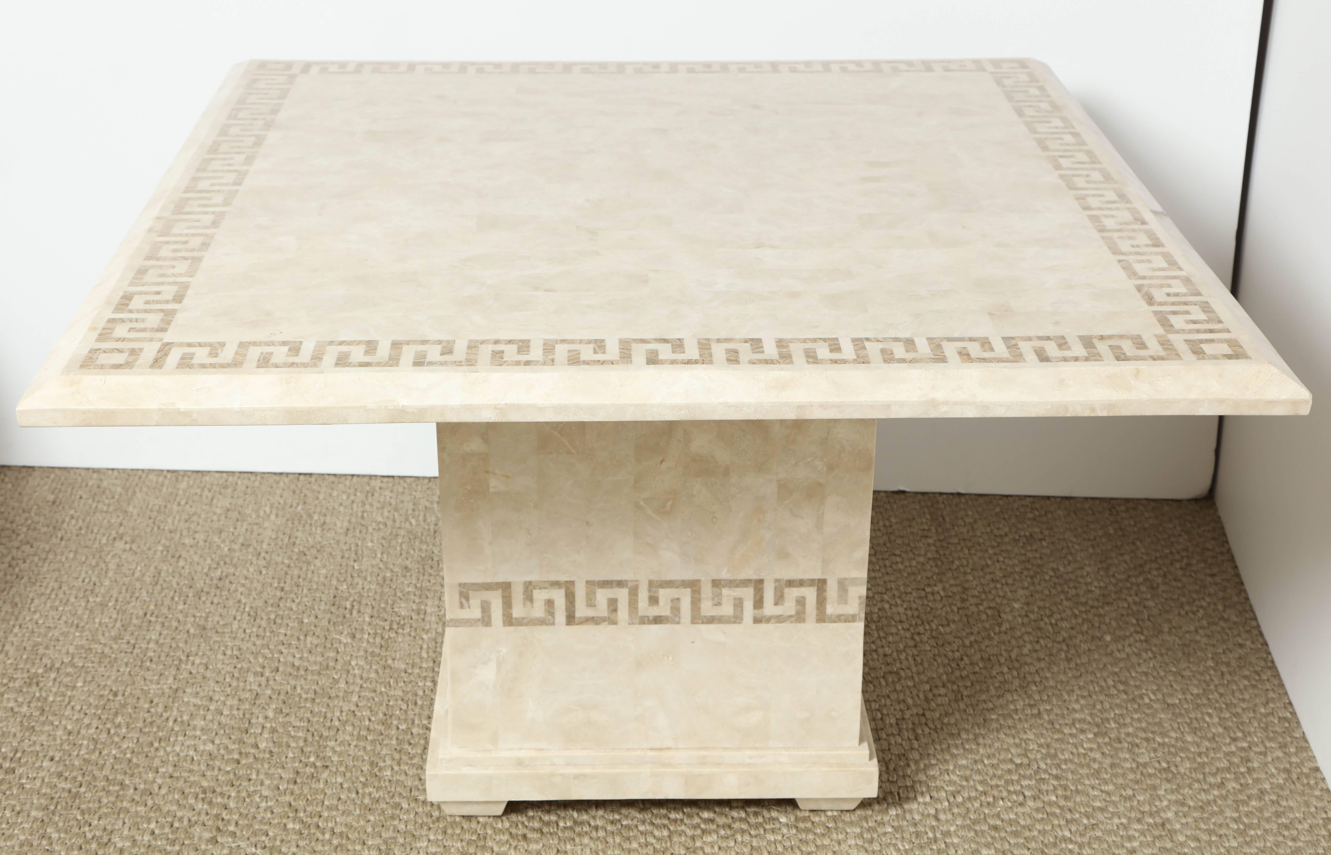 This super chic table consists of a square top with a slightly beveled edge over a square centre pedestal. It is constructed of pieces of marble over a wood base and is accented by a Greek key design on the top as well as surrounding the base. The