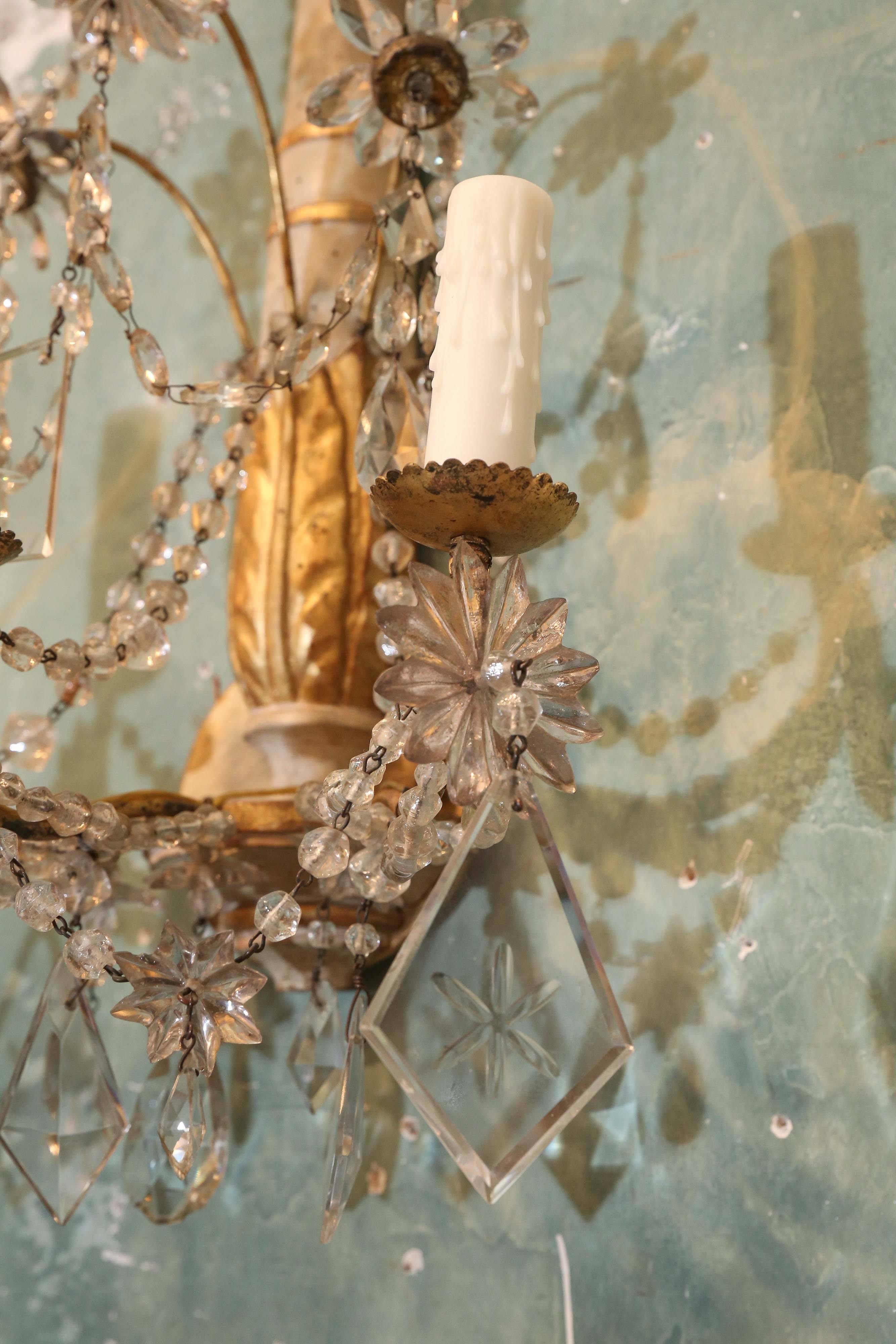 Pair of painted and gilded wood sconces with crystals. Carved leaf pattern and gilded centers to the crystal flowers.