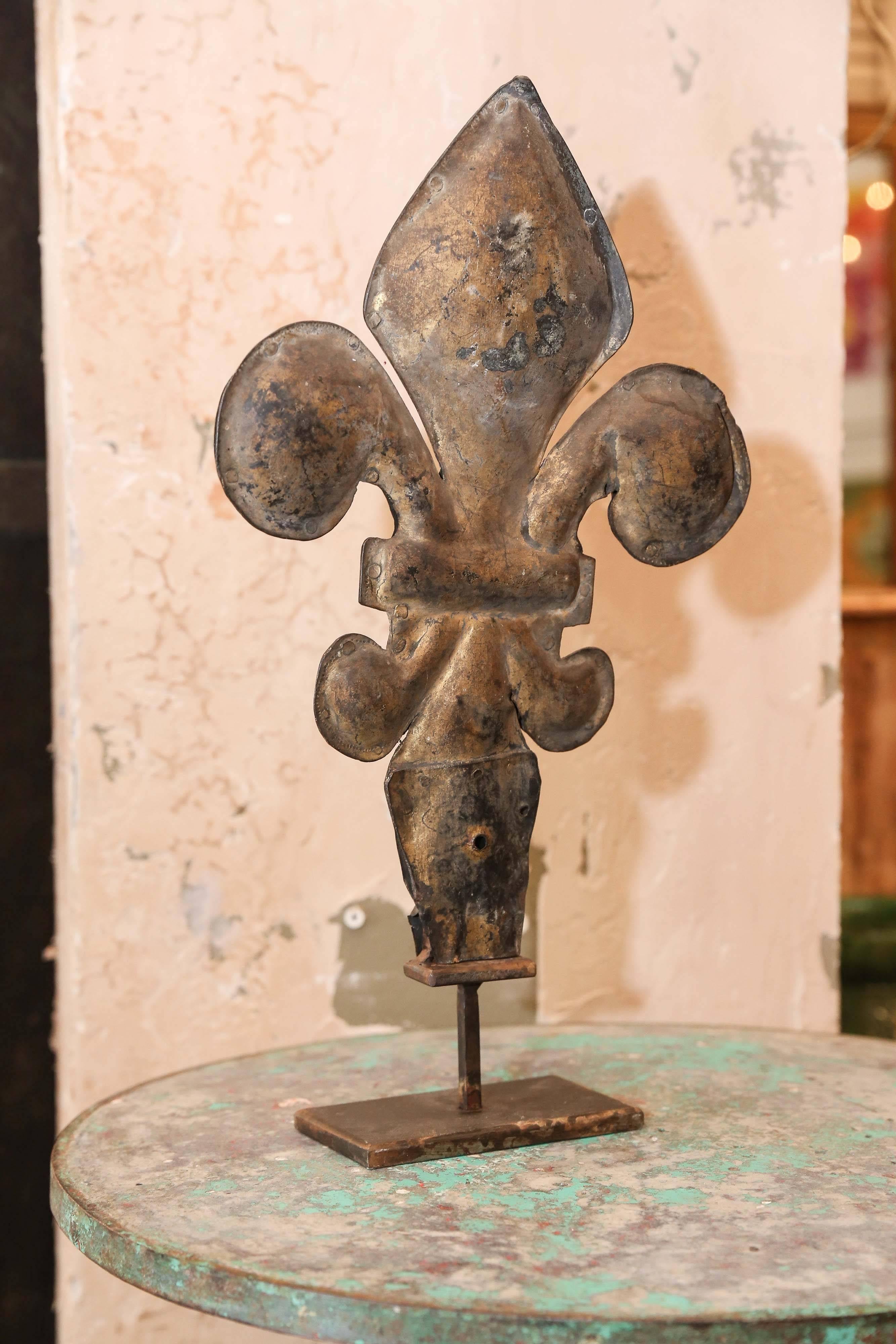 Decorative tole fleur-de-lis in gilt on a metal stand.