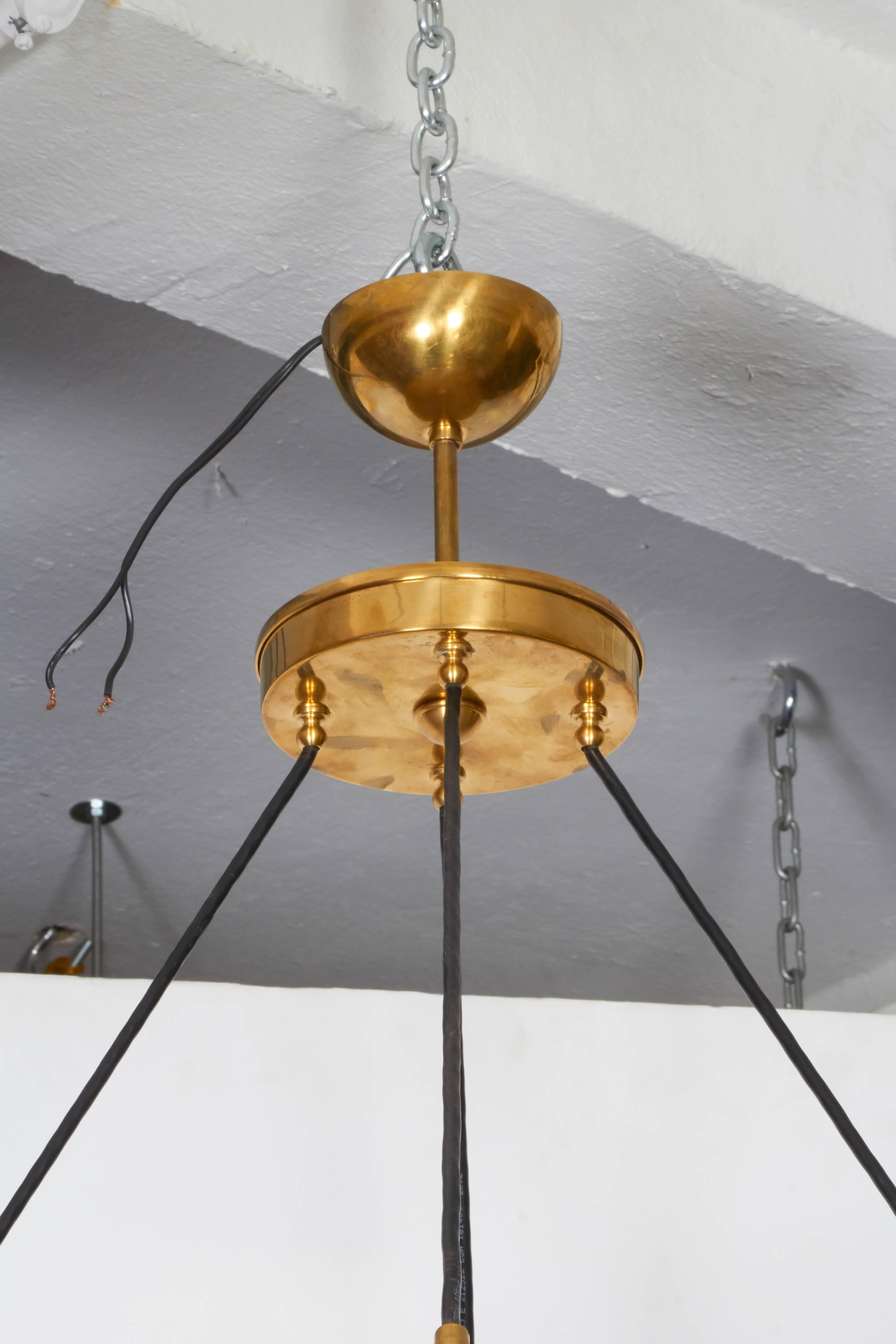 An Italian chandelier, manufactured, circa 1960s, featuring nine hanging lights with surrounding amber globes in handblown Murano glass, suspended from a ring form brass frame. Requires nine candelabra base bulbs. This fixture remains in excellent