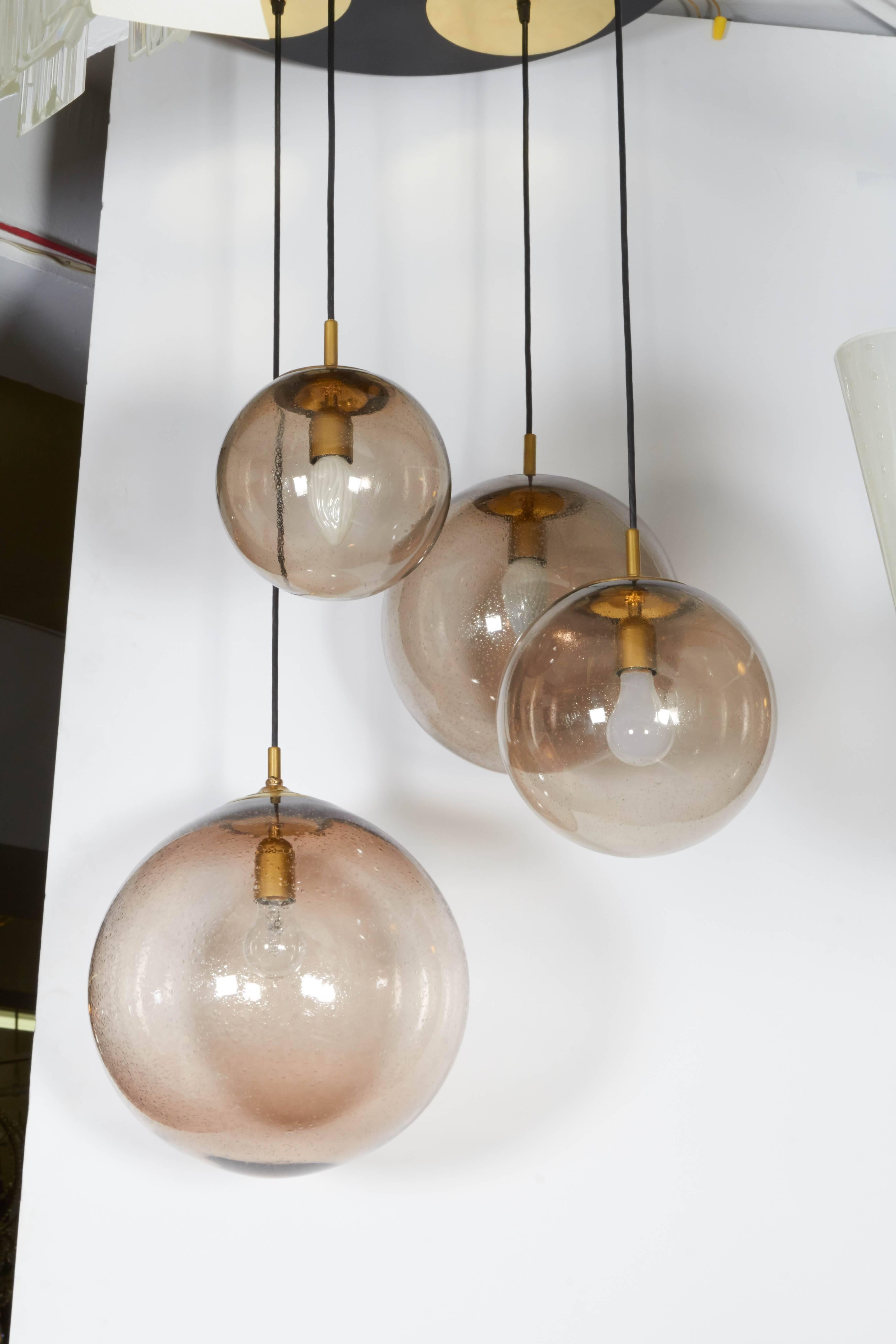 This highly modern light fixture, produced circa 1965 by RAAK of Amsterdam, Netherlands, is comprised of four hanging pendants, each with smoked glass globes of varying sizes, suspended at different lengths from a black ceiling plate with brass
