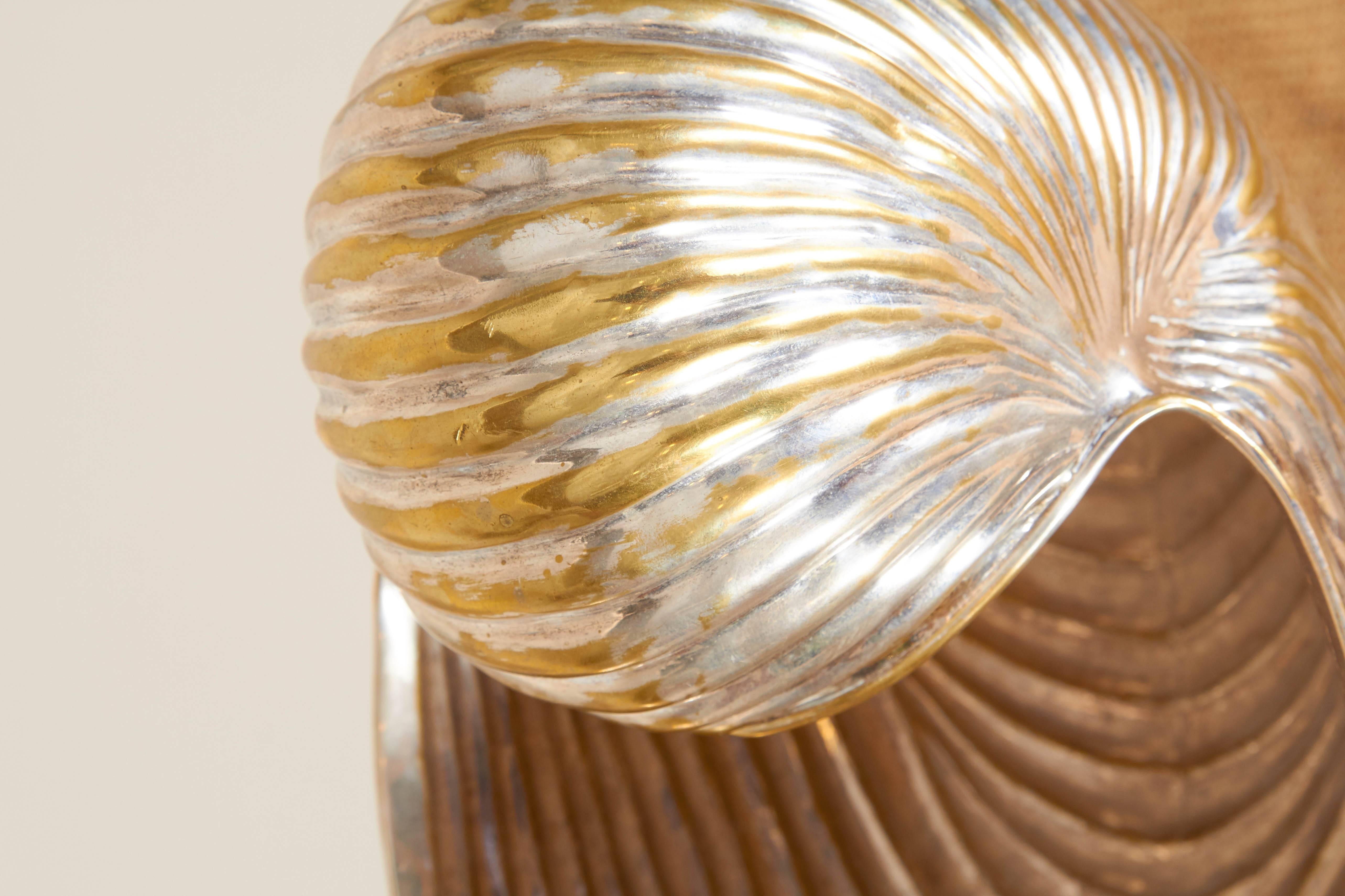 A silver plate champagne cooler in the form of a nautilus shell, supported by a faux bamboo, crossed tripod stand, circa 1960s. Shell is removable from stand, including three legs. Markings include [Los Castillo Taxco] [Placeado] [TA-01]. Overall