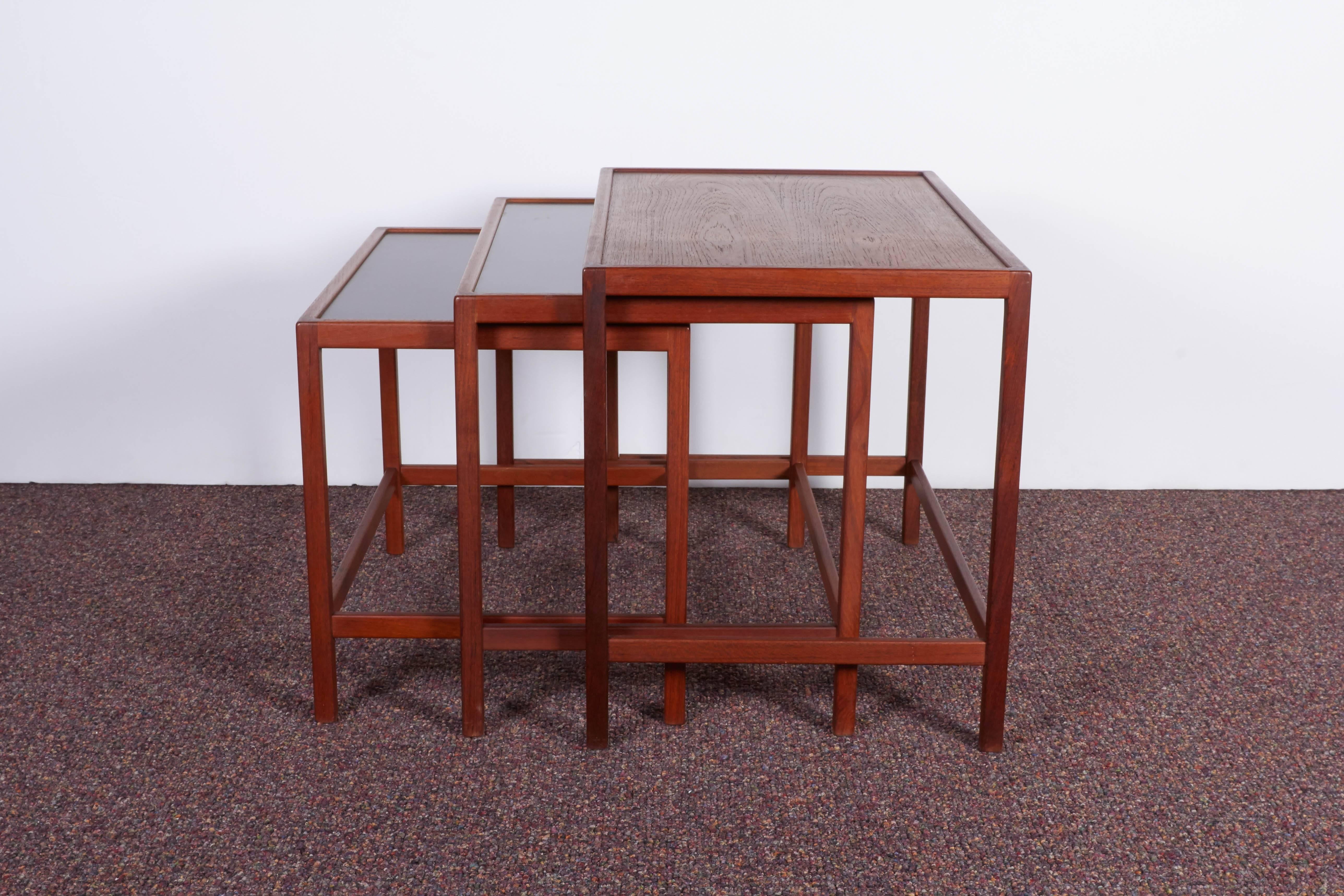 A set of three highly linear nesting tables in teakwood by designer Kurt Ostervig, manufactured in Denmark, circa 1960s, the smaller two with inset black laminate tops. All three tables remain in very good vintage condition.

Dimensions in