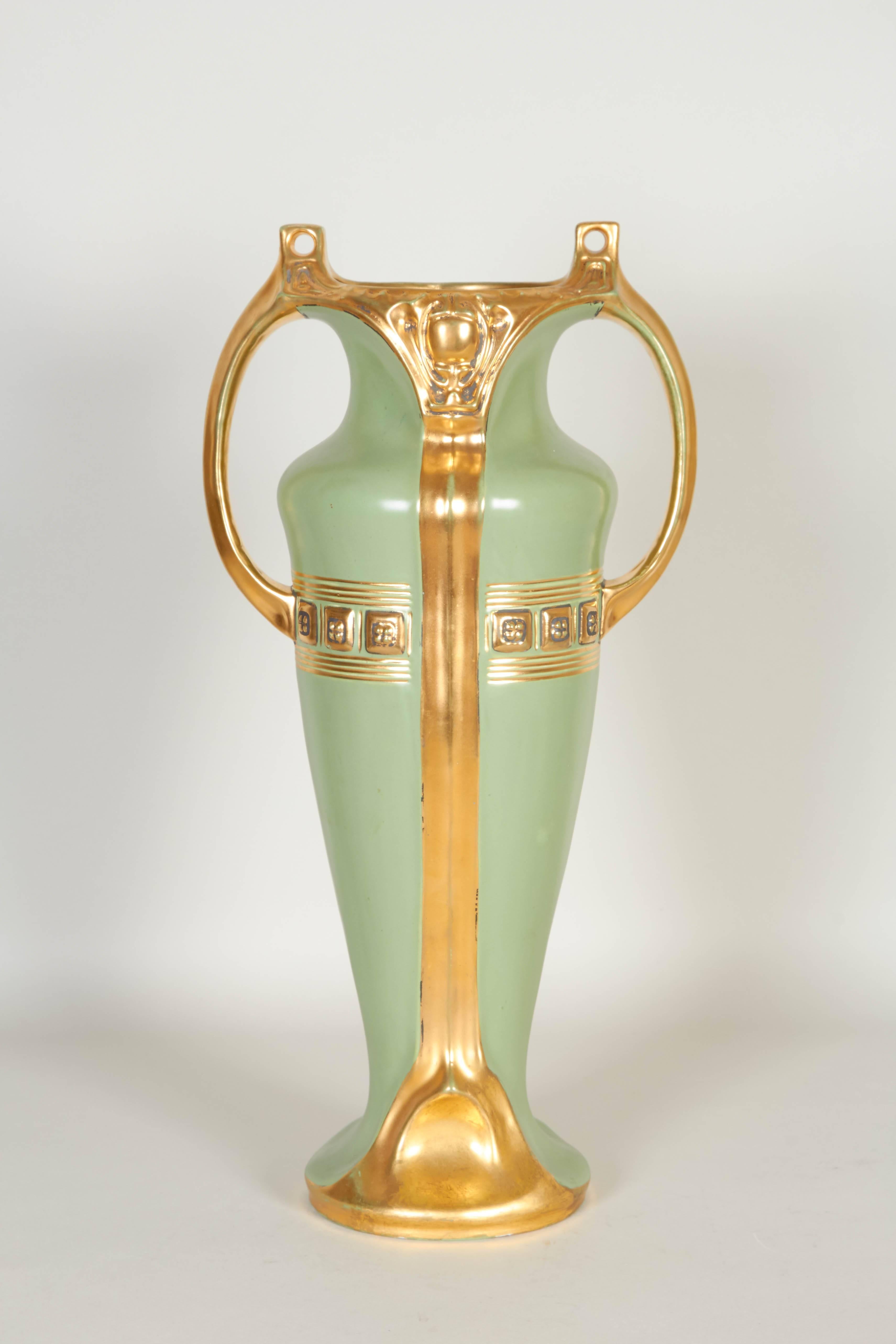 An early 20th century Austrian handled porcelain vase, designed in the Greek Revival style, urn form with green matte glaze and gilding, detailed with geometric banding and designs reminiscent of the Art Nouveau era. Markings include [Austria/ 1142]