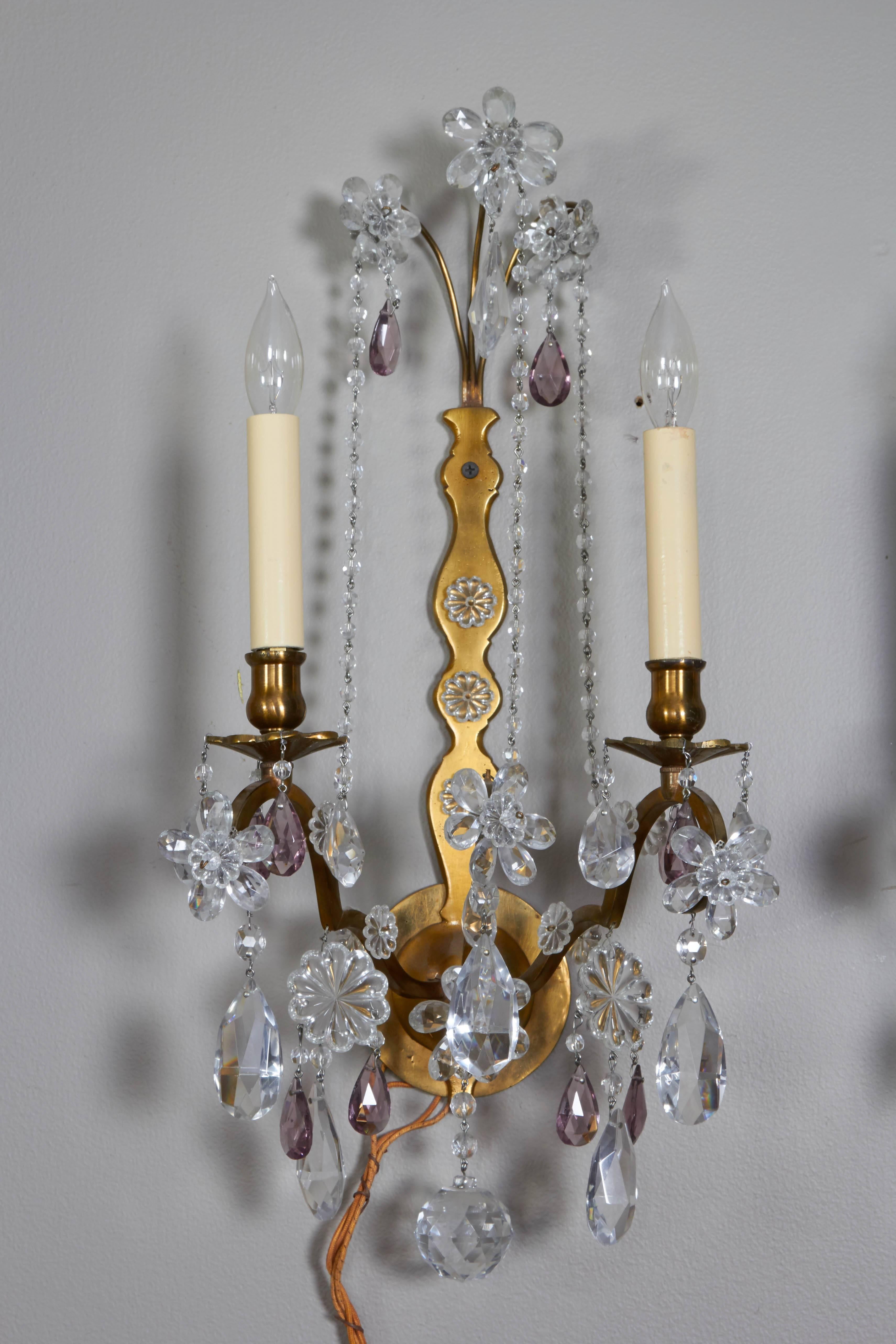 Metal sconces in a neoclassical style with crystal florets in clear glass and lavender. Two faux candles (electrified) on arms, with a central arm holding a floret. Two pairs available; may be sold in individual pairs

 