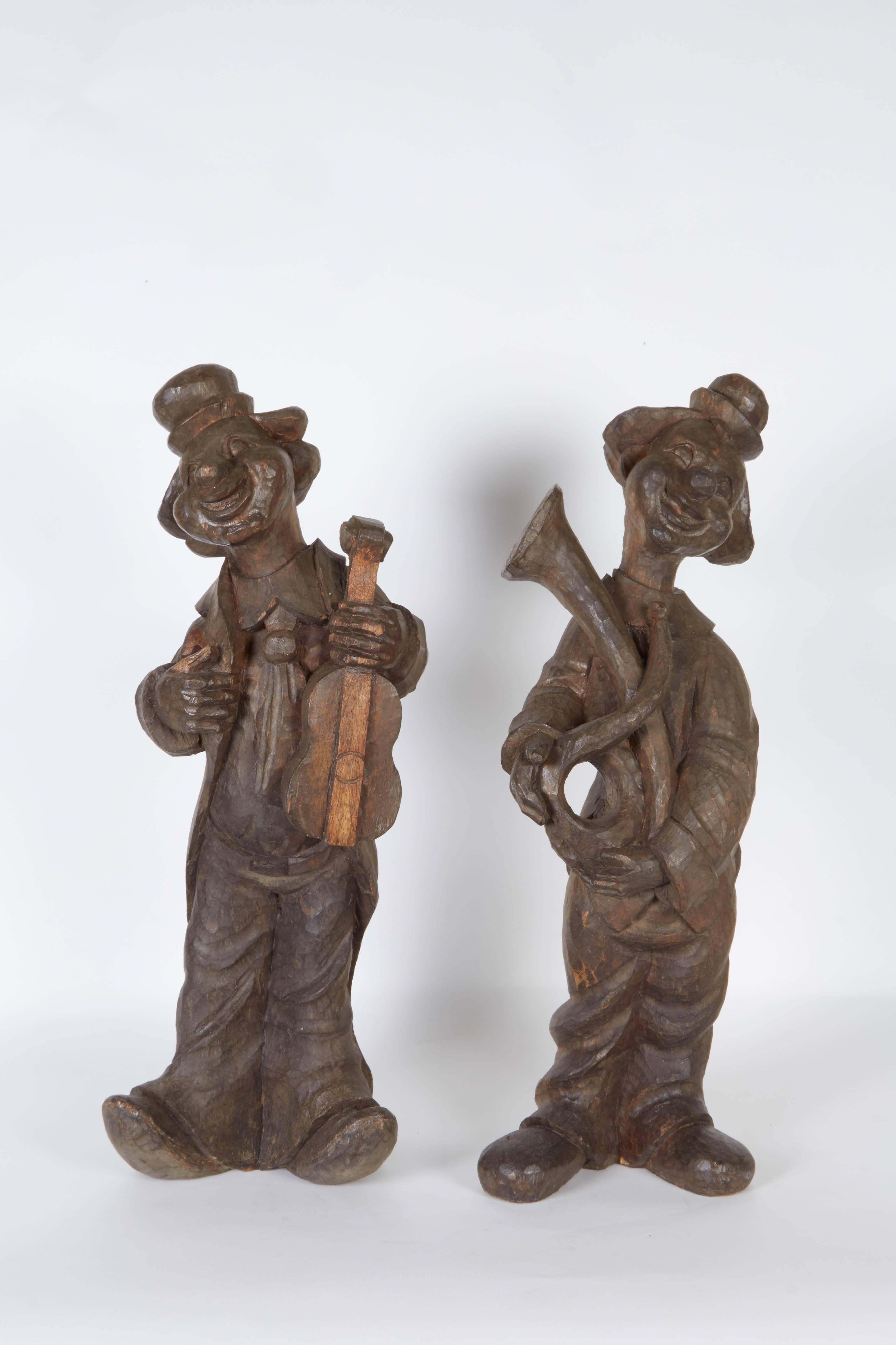 A pair of vintage figures of clowns, produced circa 1920s by a master carver in the Philippines, originally intended as papier mâché molds, each carved from solid wood, the figures bearing a violin and horn. Despite minor presence of wear, including