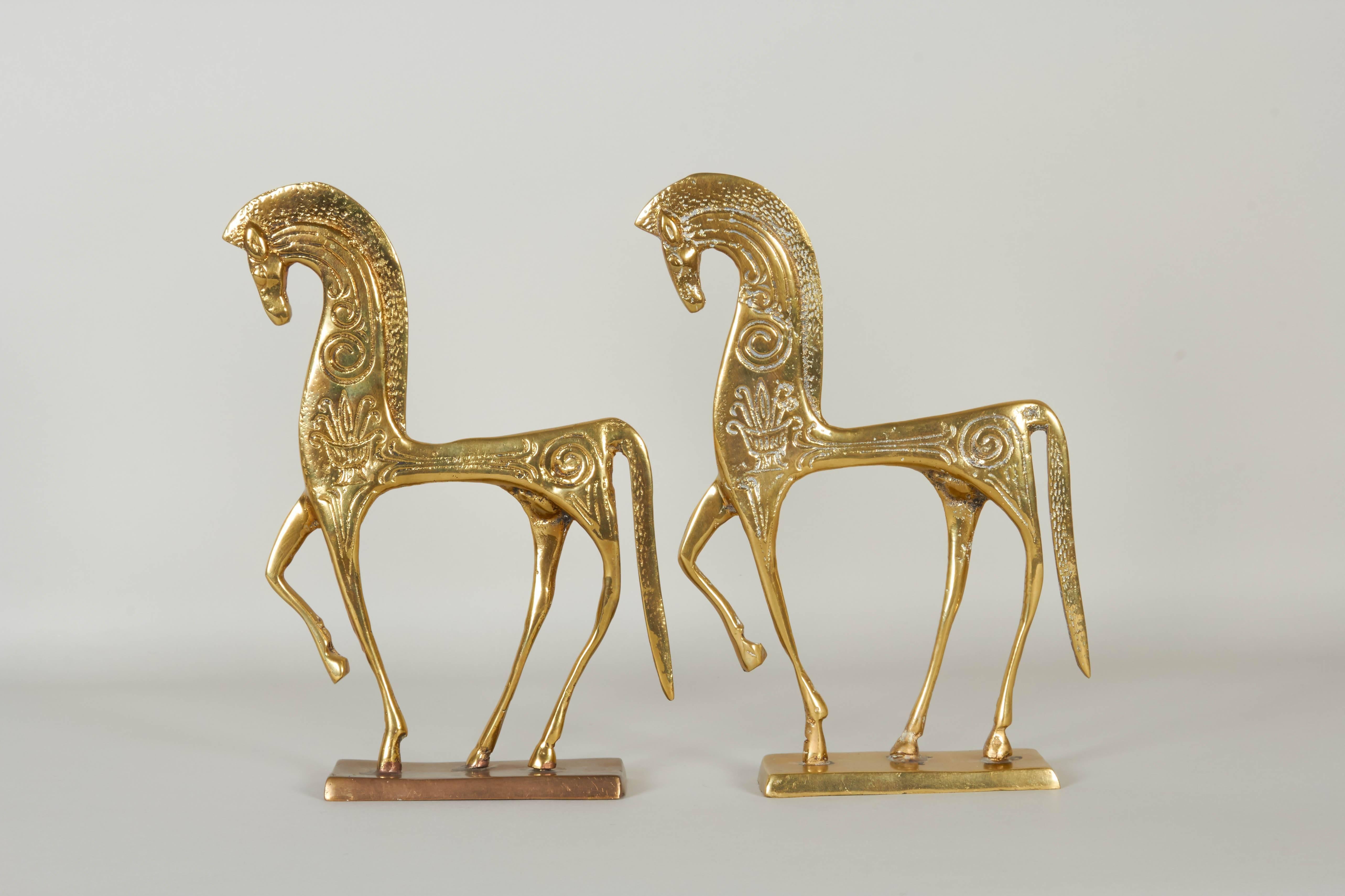 A pair of vintage Etruscan horse figurines in brass by designer Frederic Weinberg, each modeled flat, decorated with swirling patterns, mounted on rectangular bases. The figures remain in very good vintage condition, with presence of age appropriate