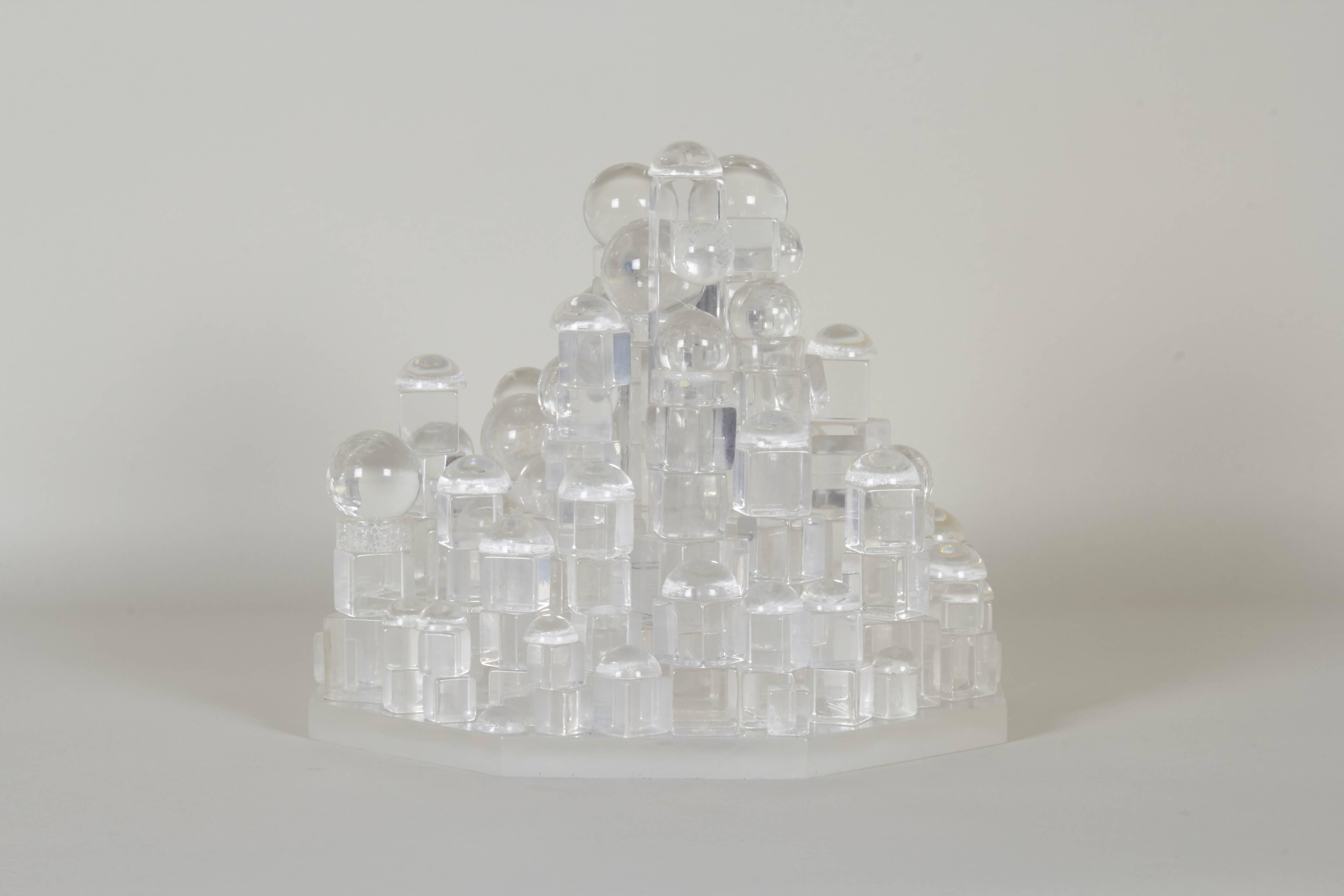 A small scale abstract sculpture in Lucite, produced circa 1970s, comprised of geometric forms, including cubes, balls and hemispheres, affixed to octagonal base. Despite minor crizzling and presence of repairs, this piece remains in good overall