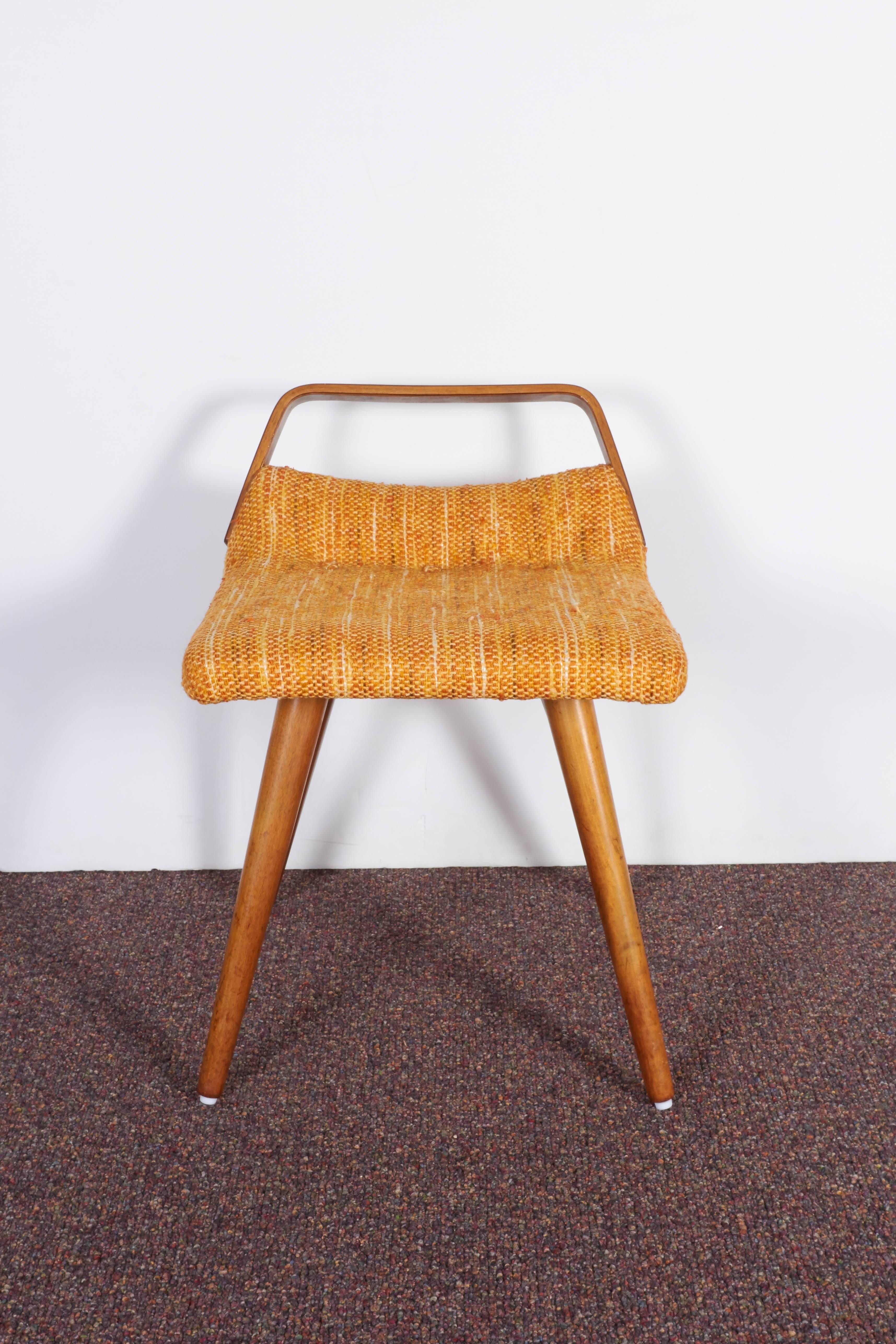 A dressing table stool, designed in the style of Dunbar, produced in the United States, circa 1960s, upholstered in the original warm colored woven fabric, against curved seat with bentwood back rail, raised on round tapered beech legs. Very good