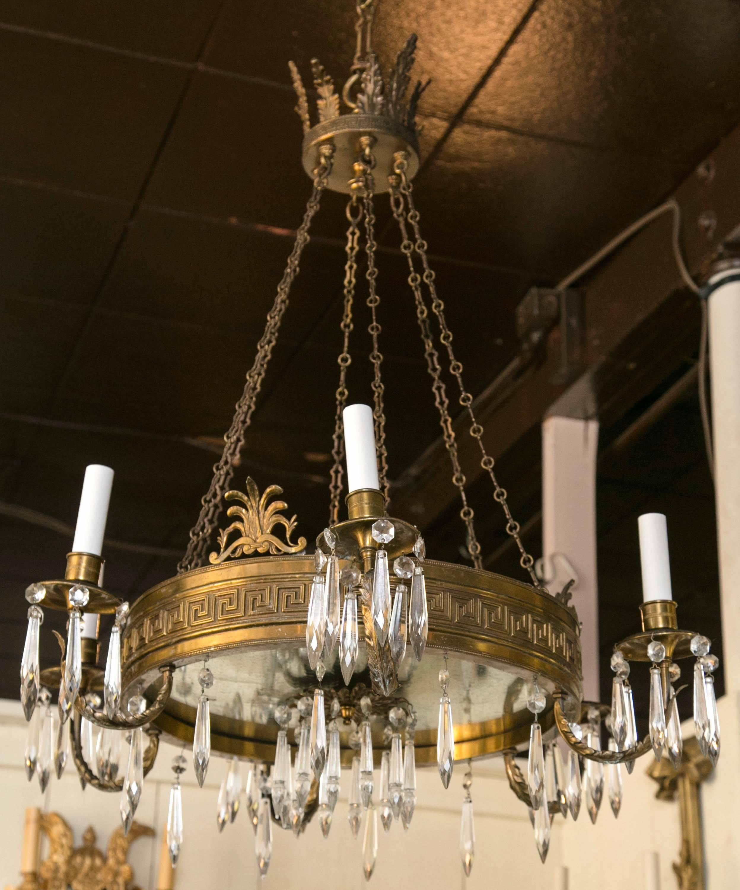 Topped with a crown of acanthus leaves. The six chains connect to a ring of brass decorated with a Greek key motif. Six candle arms and three palmettes attached to the ring. Cut-glass drops hang from the ring, the baubeches, and the central
