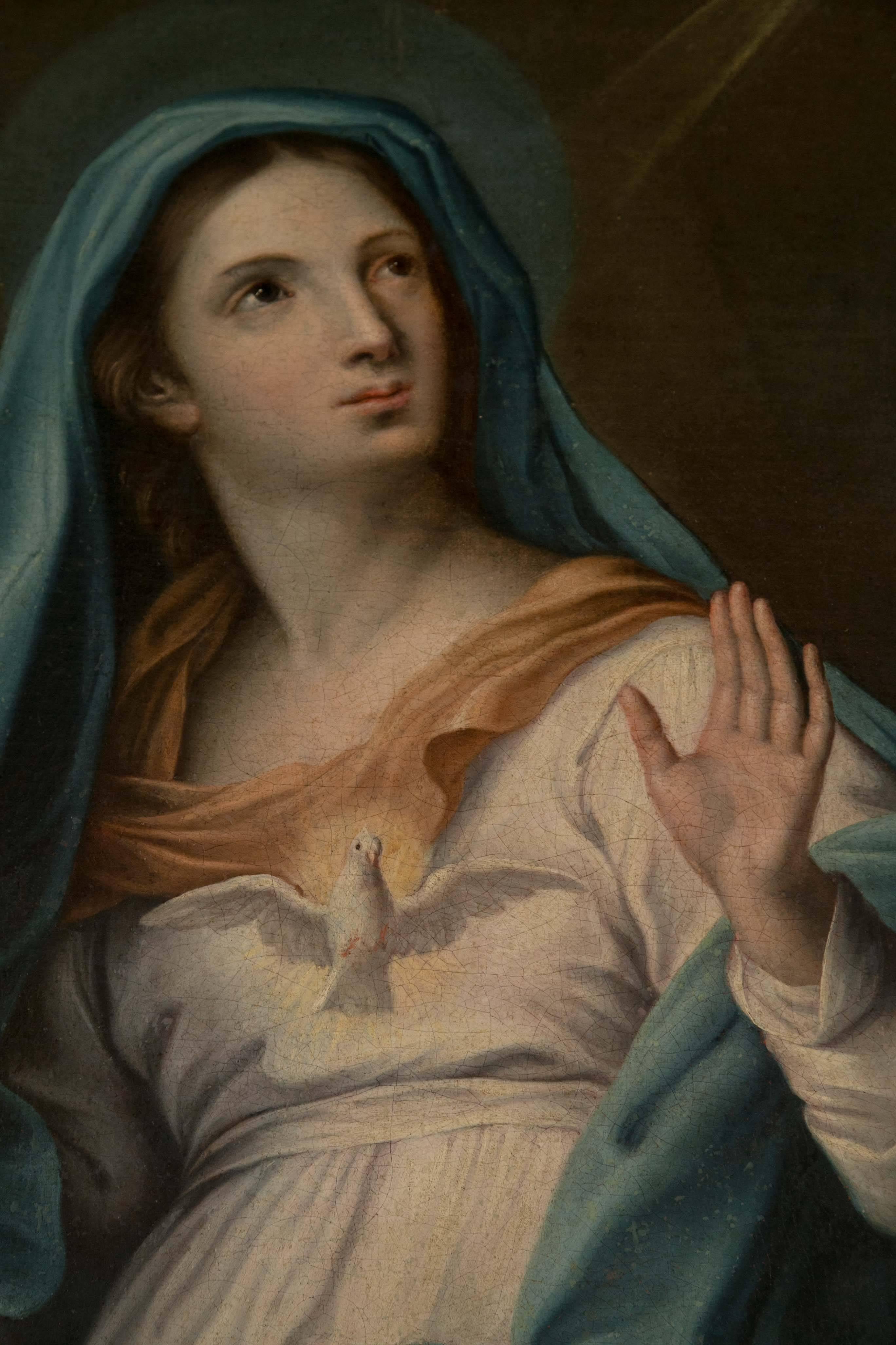 The virgin wearing a light blue shawl over her head and shoulders, wrapping in her arms. A salmon colored scarf over a white gown. The dove of the Holy Spirit centered between her hands.
The antique silver leaf frame has wear.