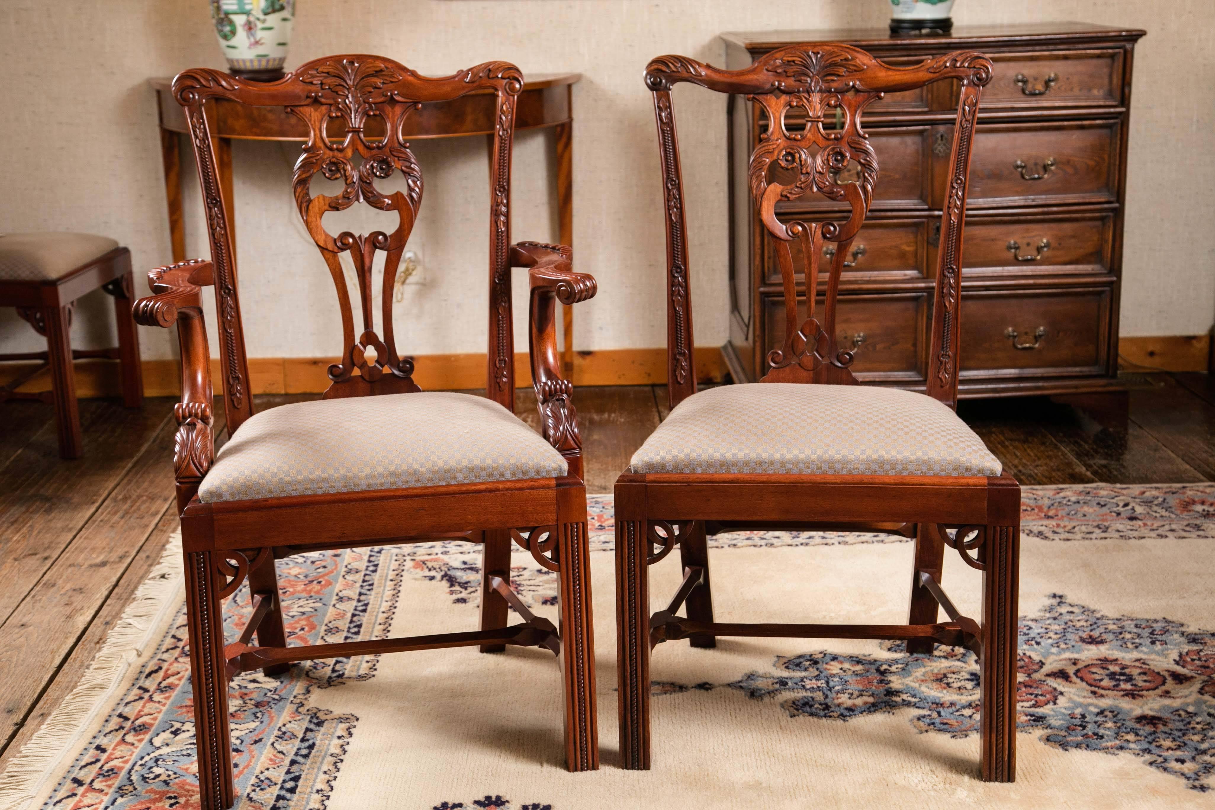 Set of 12 (two arms / ten sides) intricately carved mahogany dining chairs. These Irish Chippendale style dining chairs are the epitome of fine reproductions. From the acanthus themed carvings on the crest rail and splat to the leg brackets and