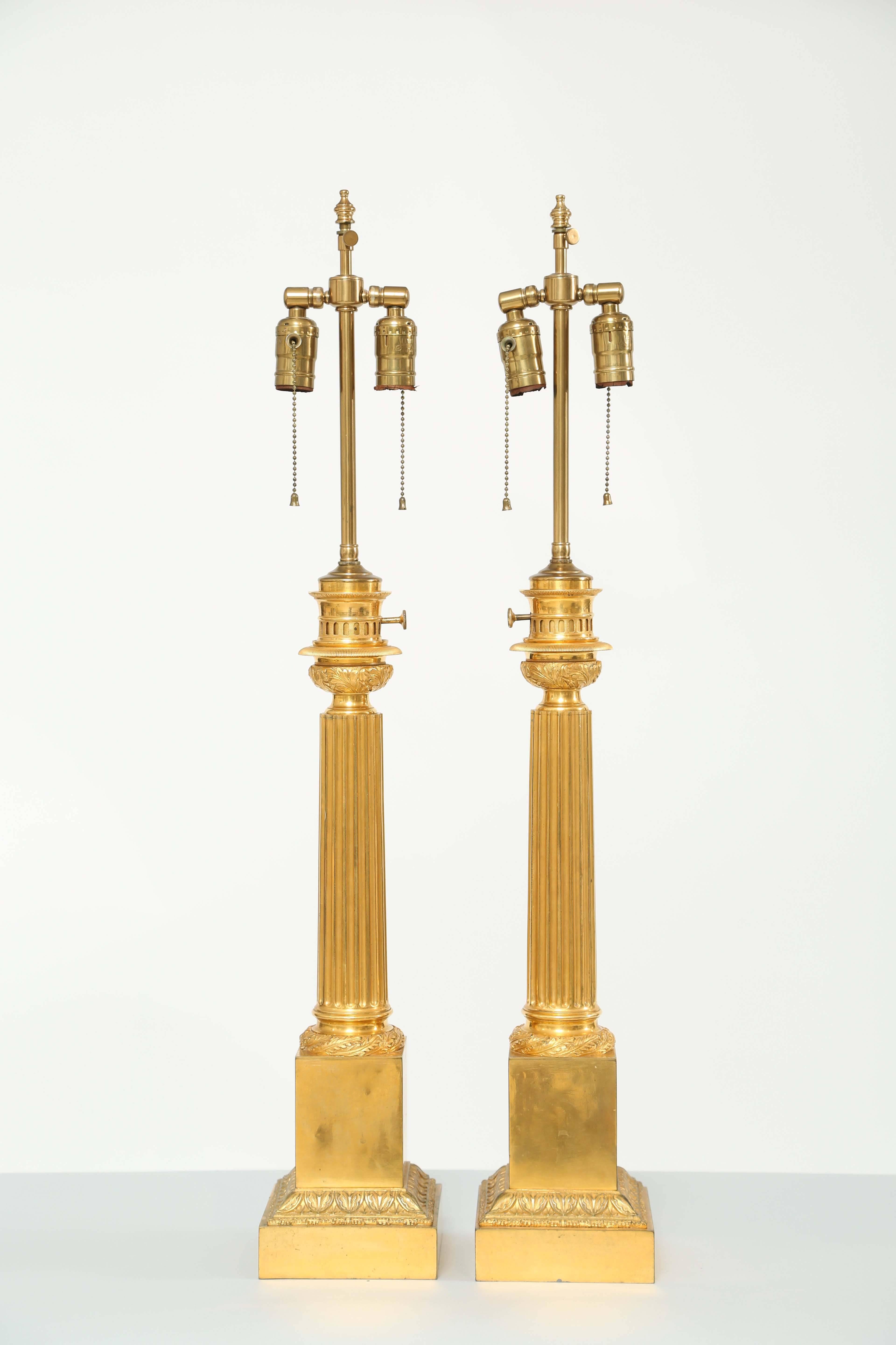 Fine pair of lamps, of gilt bronze, each a fluted tapering column, with foliate capital, on round foot decorated by laureling, raised on square plinth to its graduated base, adorned with palmettes. Labeled 