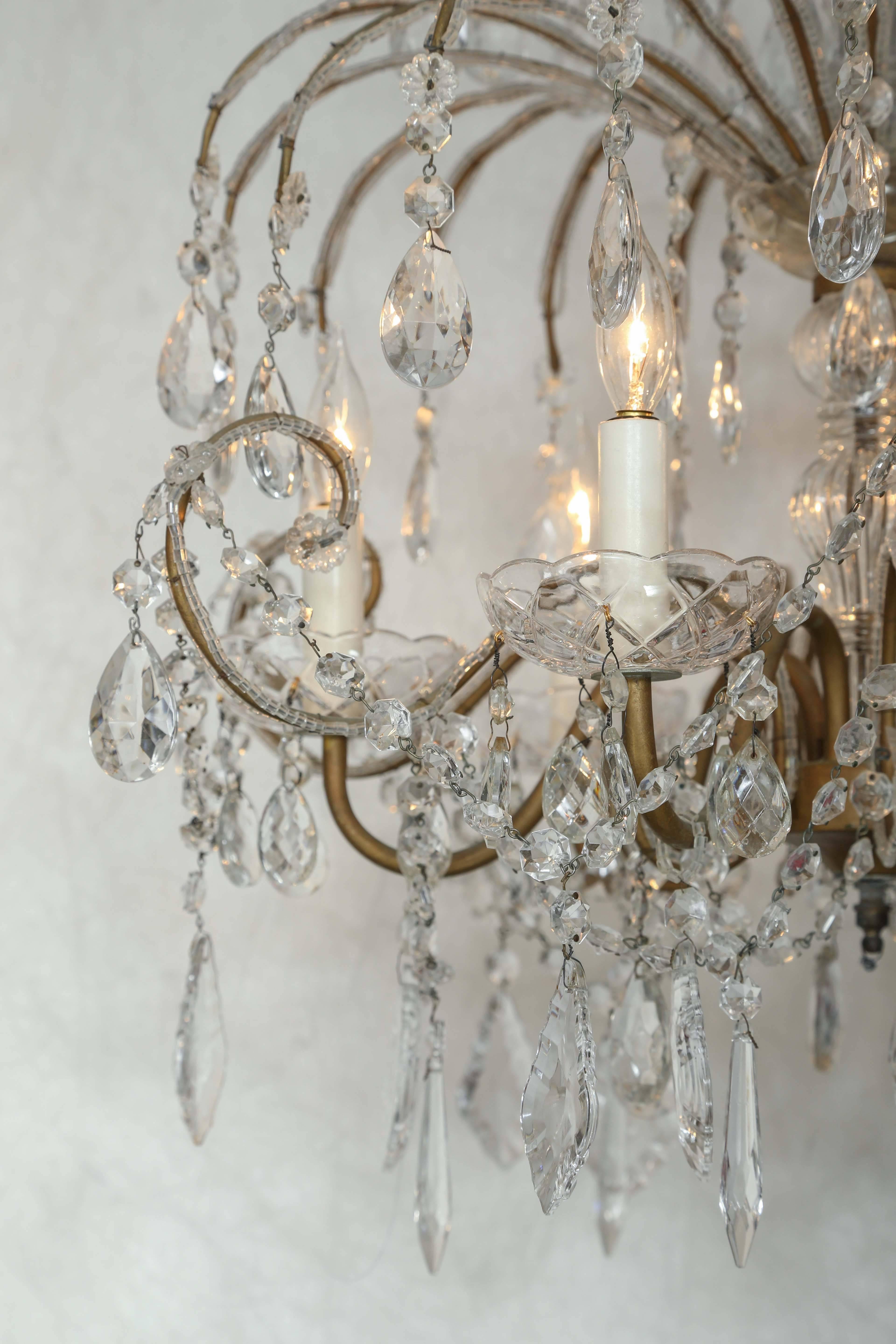 Chandelier, having a gilded iron frame encrusted with crystal beads, with six S-scroll candle arms, surmounted by three graduated tiers, ending in faceted drops, the entire fixture draped with swags of crystal strings.

Stock ID: D9383