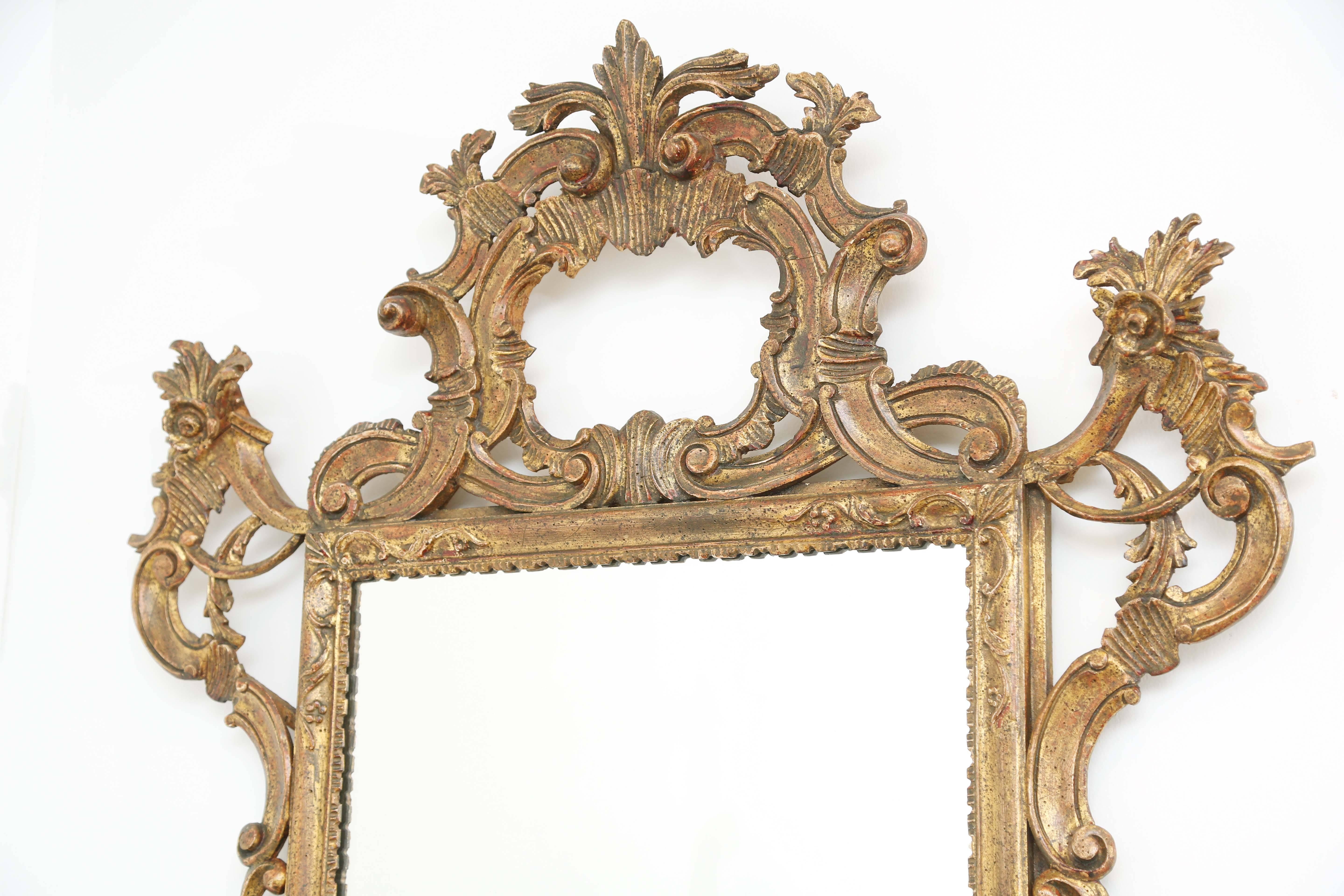 Wall mirror, having a rectangular gadrooned frame, surmounted by a pierced pediment of elaborate foliate scrollwork, accented by coquillage and rosettes, with similar pierced embellishments on its corners and base.