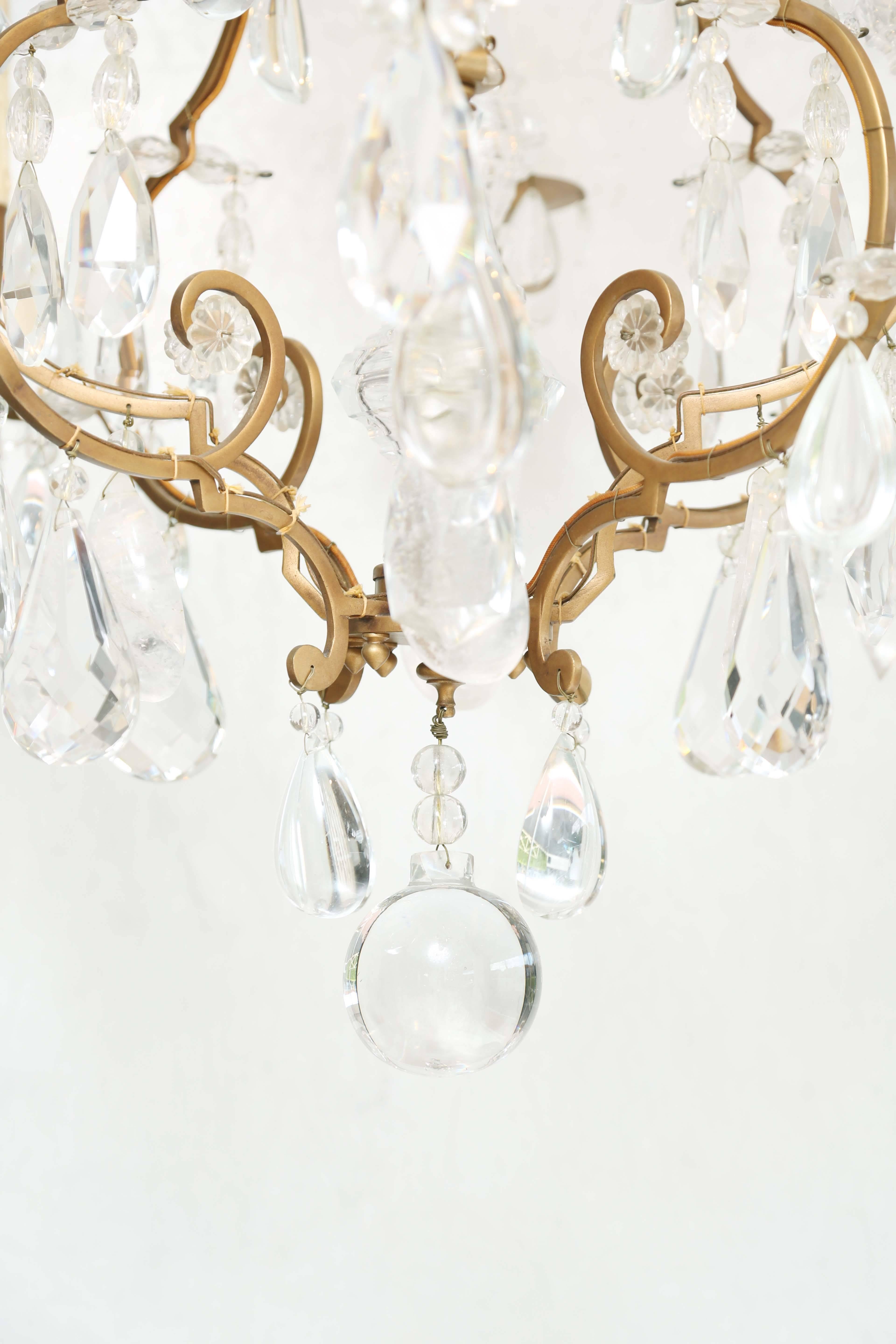 Chandelier, in the Louis XV taste, having a gilt bronze frame set with an interior rock crystal finial and mounted eight scrolled bronze candle branches, on two-tiers, hung with faceted, clear and rock crystal drops and flower heads, accented by cut