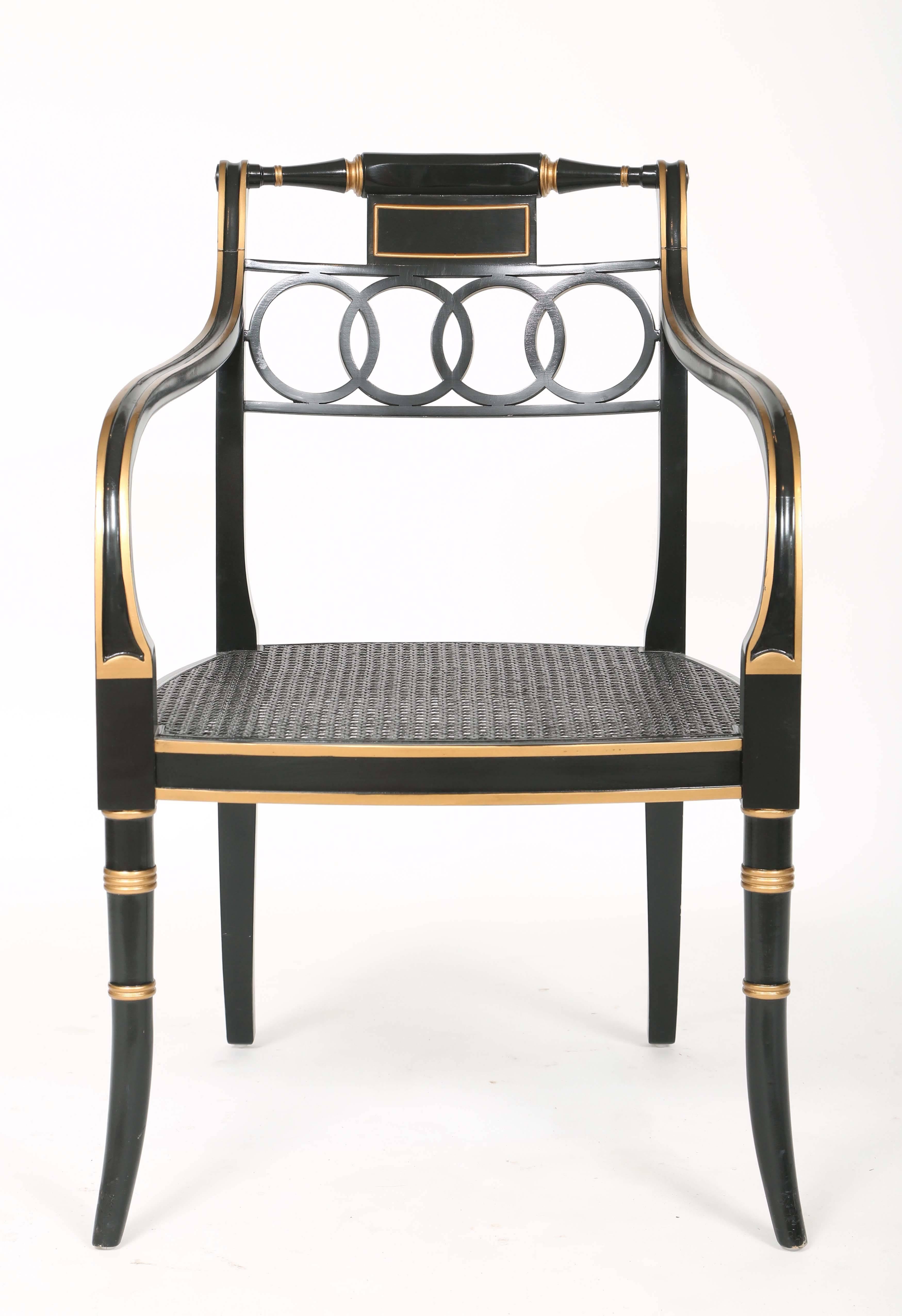 Pair of open armchairs, each chair in black lacquer with gilt accents, its curved back splat flanked by turned rails, over linked rings, to its downswept arms joining the caned seat, raised on round, tapering, splayed legs.

Stock ID: D2294