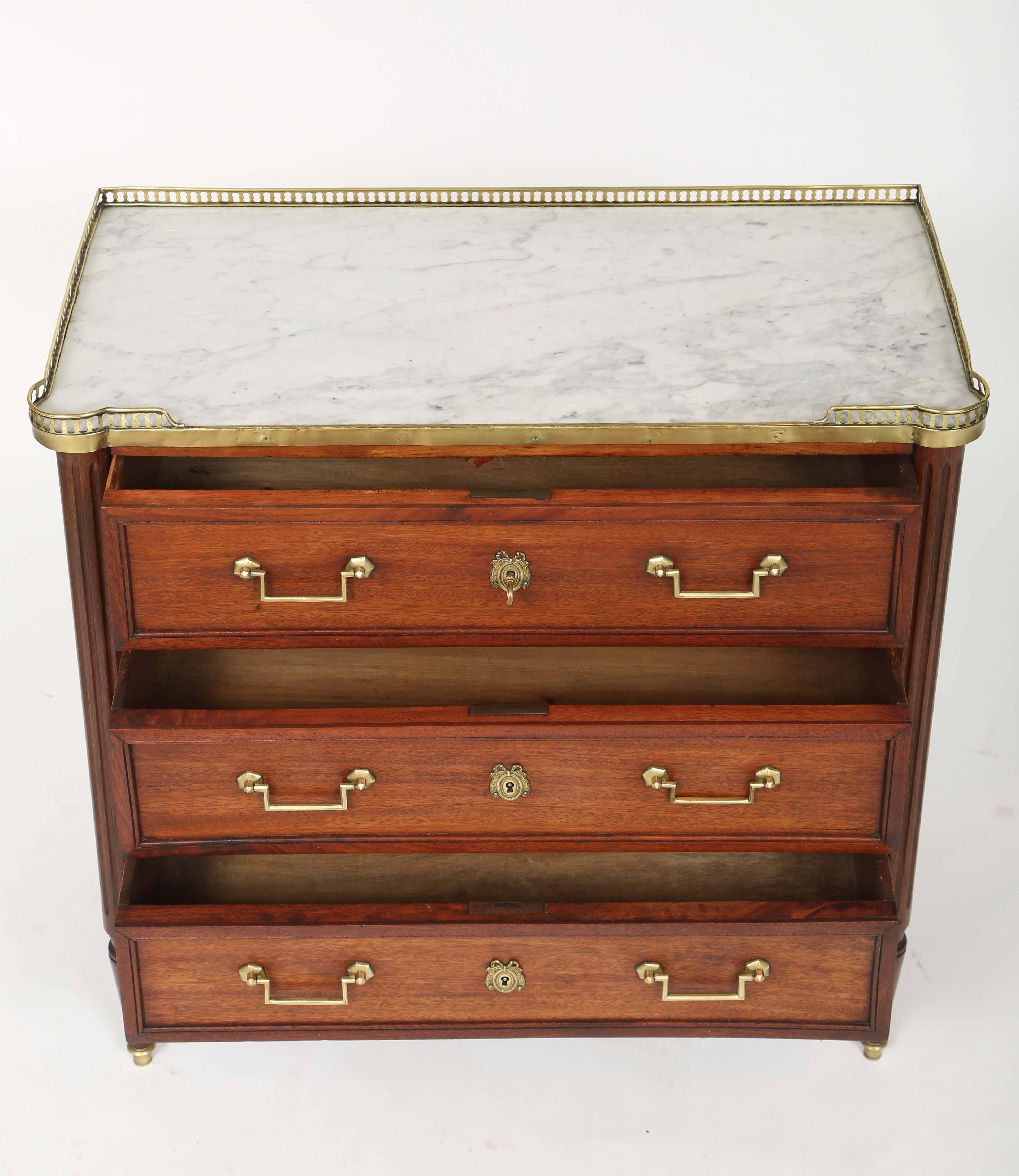 Louis XVI style mahogany and marble-top hall chest, having a rectangular marble top with turreted corners, under a pierced 3/4 gallery of brass, on a conforming case fitted with three long drawers, all paneled and with brass banding, raised on