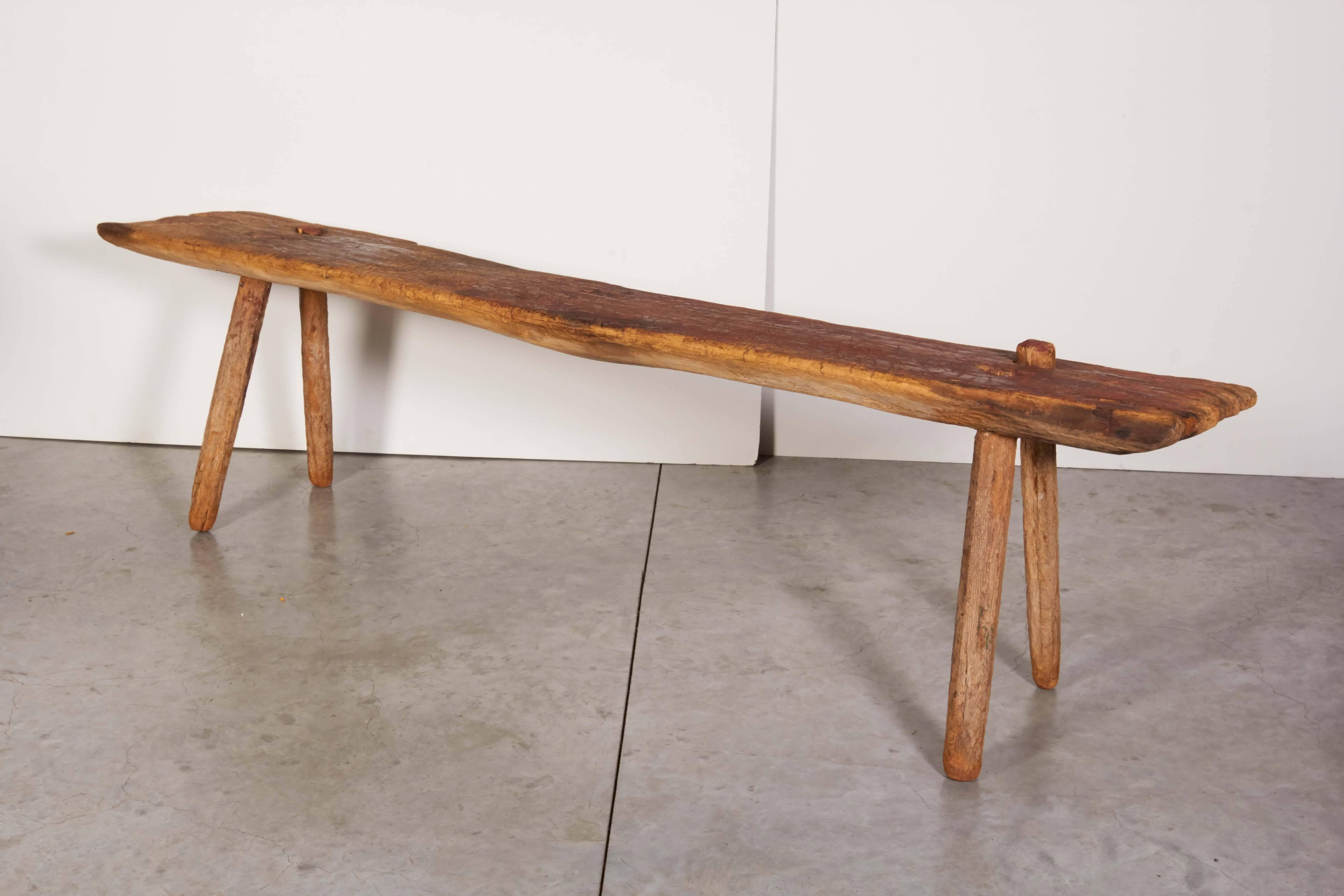 An incredible and unusual Primitive bench with a thick seat, simple legs and a wonderful faded red color that can only be created by years outdoors in the sun. The long seat is very thick, shows the hand of the maker and the impact of time on this