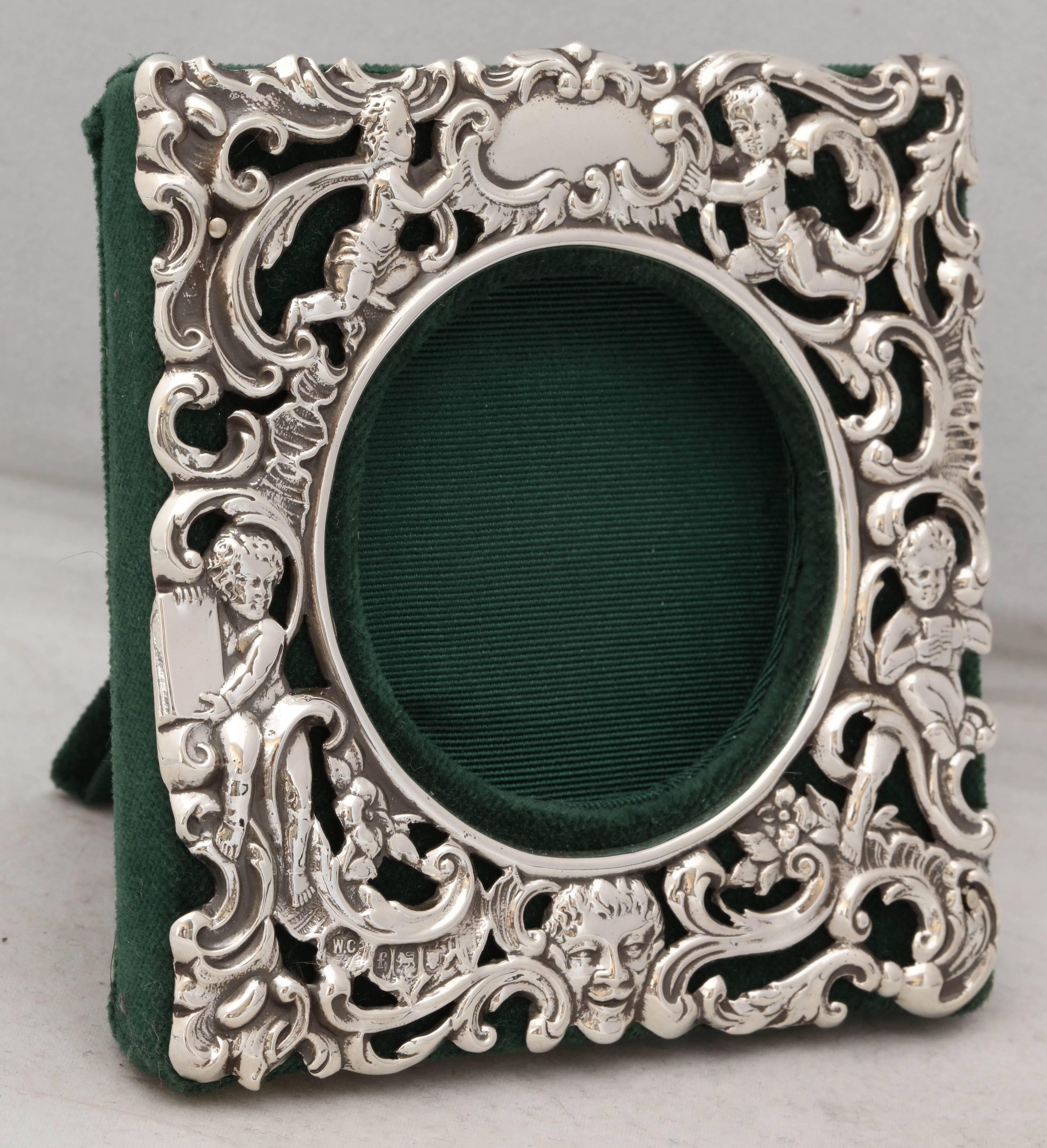 Victorian, sterling silver picture frame, London, 1901, William Comyns maker. Decorated with cherubs and swirls and having a face at the bottom. Vacant cartouche. Backed in dark green velvet. 4