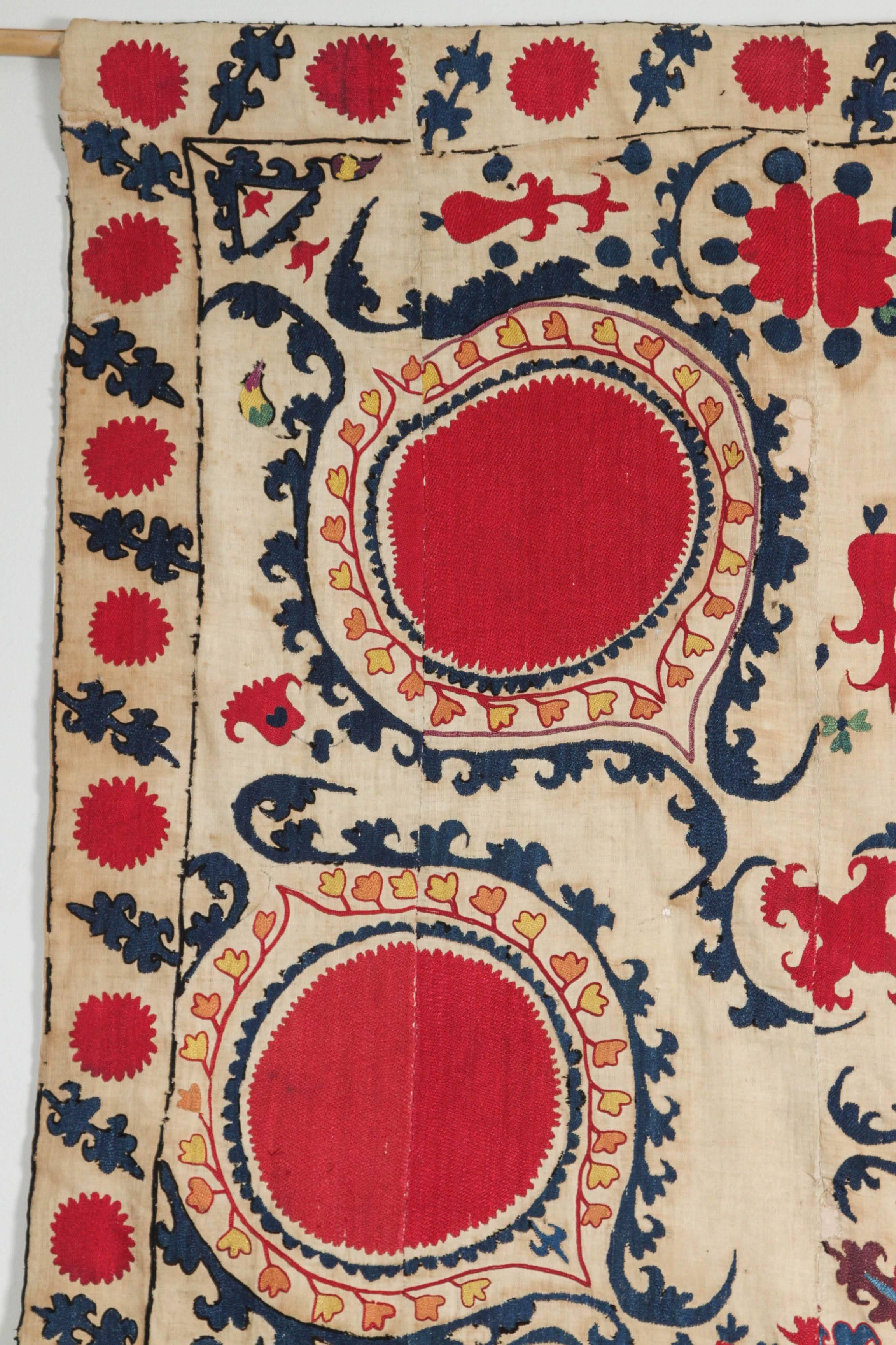 19th century Suzani textile. Silk floss thread embroidery on natural linen field. Backed with white cotton with a sleeve at top for hanging. Shows it's age in terms of condition and some staining. Check photos. Dark pink, red, blue, teal, and green.