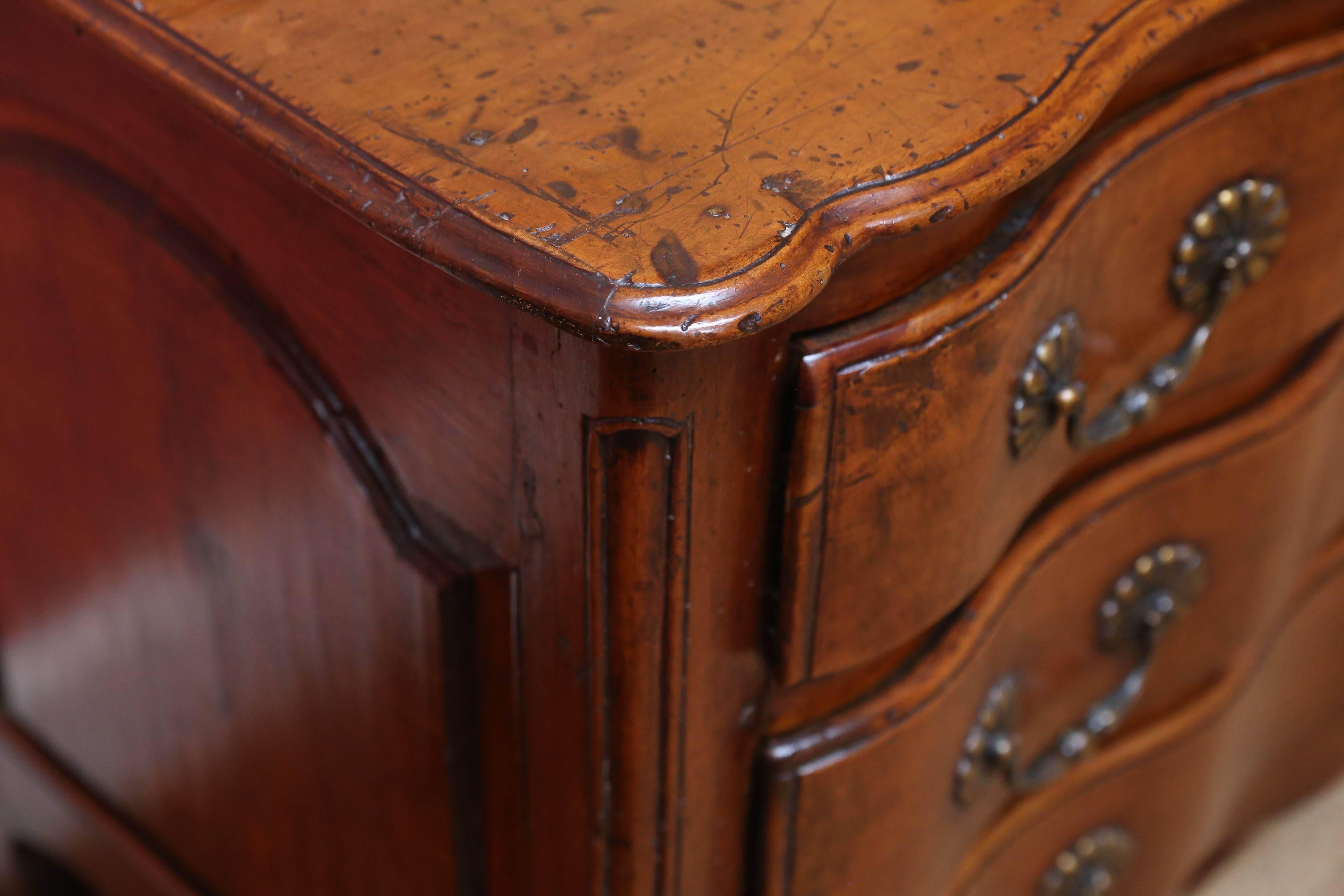 Spectacular 18th century walnut commode with three drawers and original hardware. Each drawer follows the lines of the top of the piece and have been carved out of a single piece of wood to produce the wavy pattern seen.