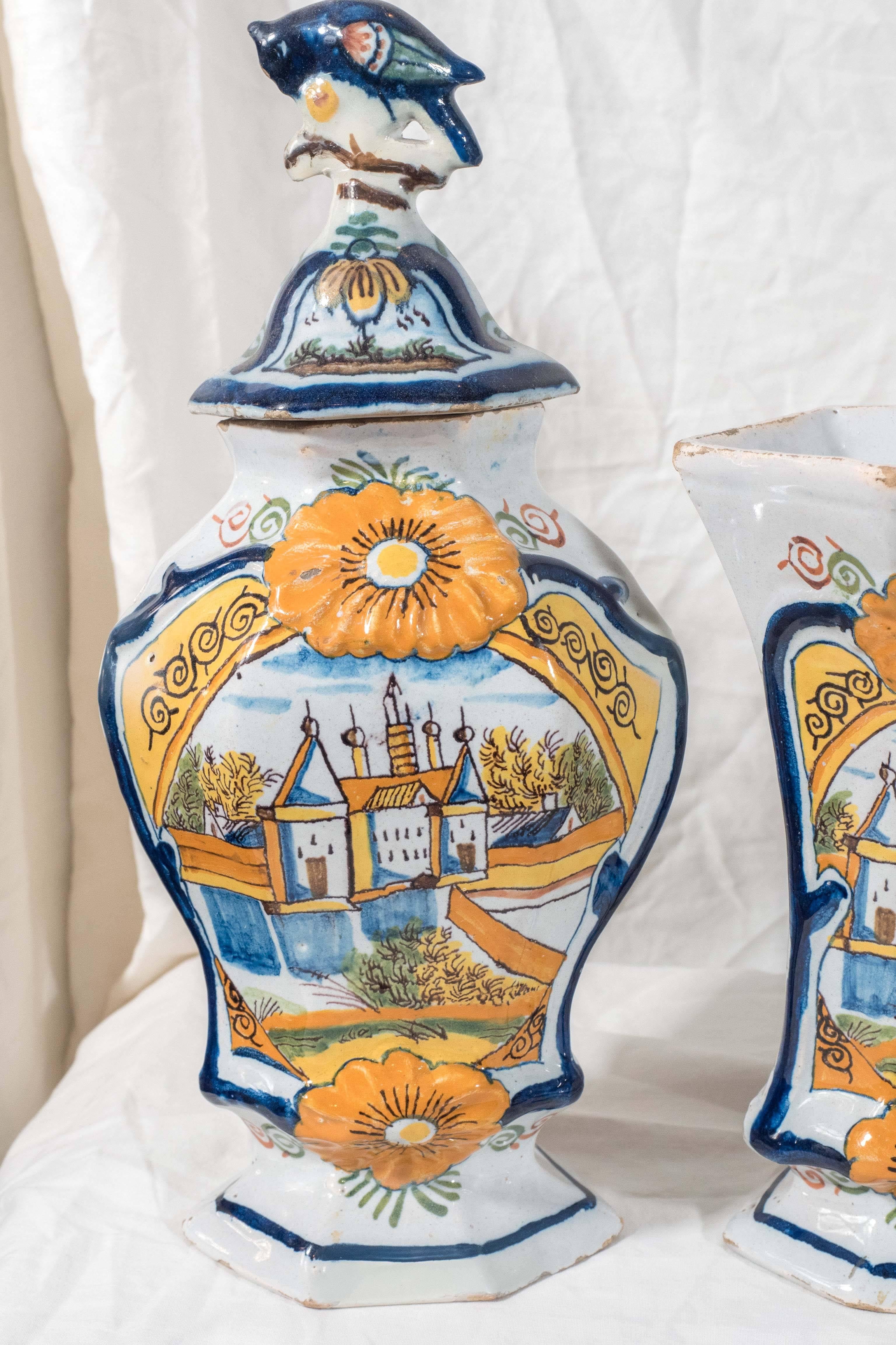 A garniture of five Dutch Delft mantle vases made in the last quarter of the 18th century.  Each vase shows a castle painted polychrome colors of bright orange, yellow, with soft greens. The image is framed by two very large sunflowers and a cobalt