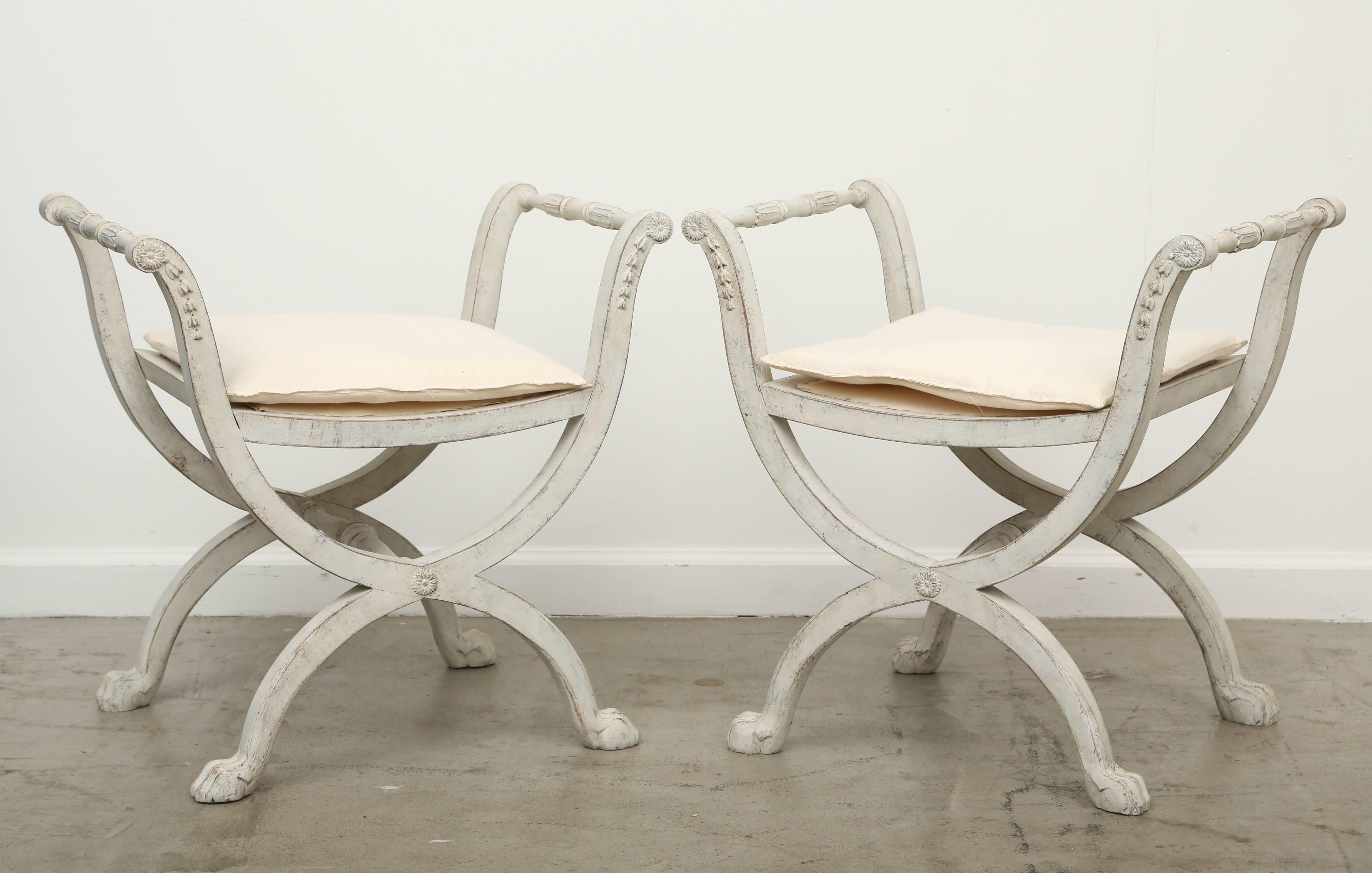 Pair of antique Swedish Gustavian X base stools early 19th century.
Benches have curved and carved arms, upholstered seat with loose cushion, X base with curved legs and paw feet, carved stretcher, grayish white distressed painted