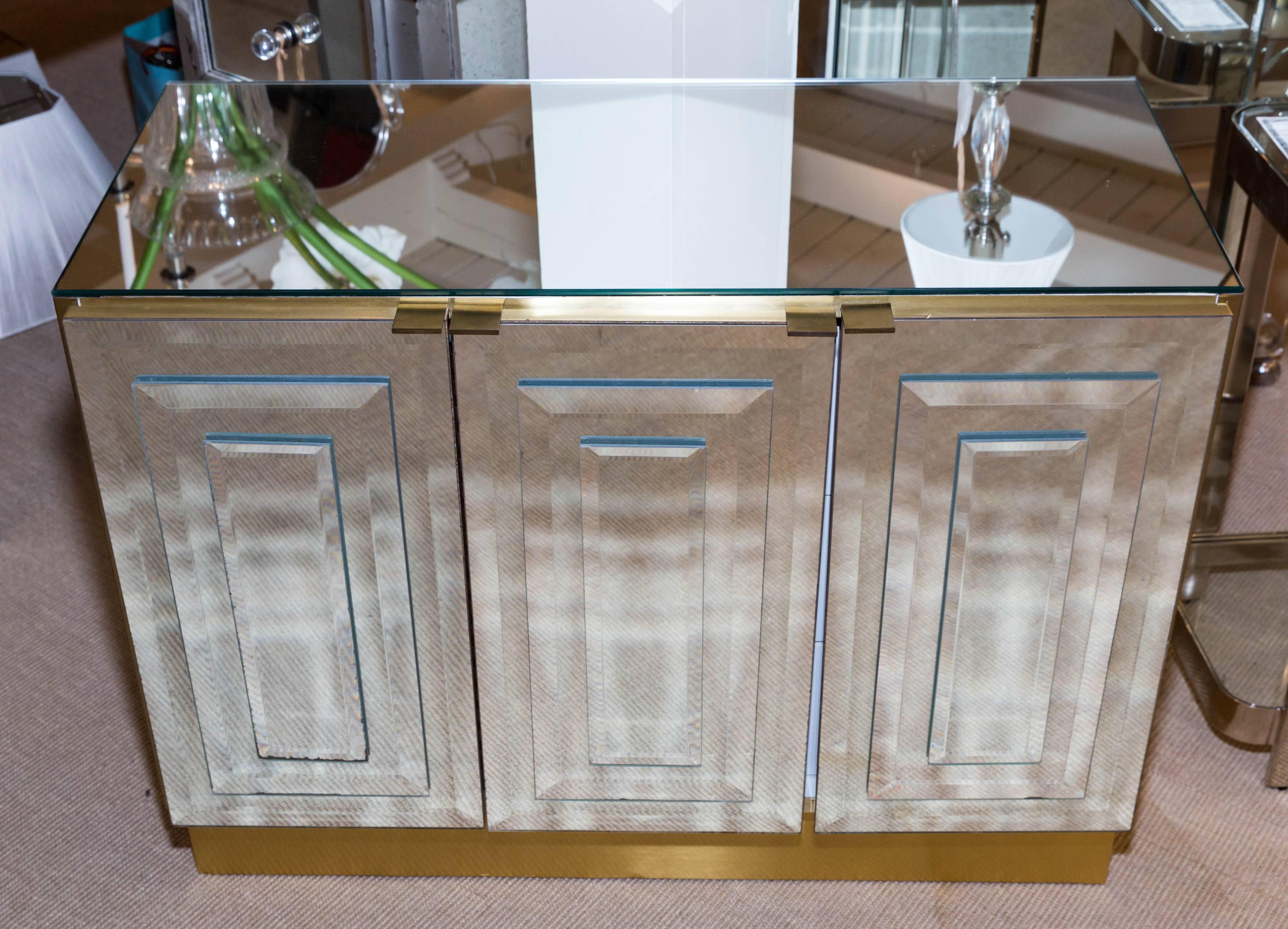 Attractive small buffet with three-mirrored doors but Ello Furniture Company The top is mirrored and the sides and base are brass as are the door pulls.