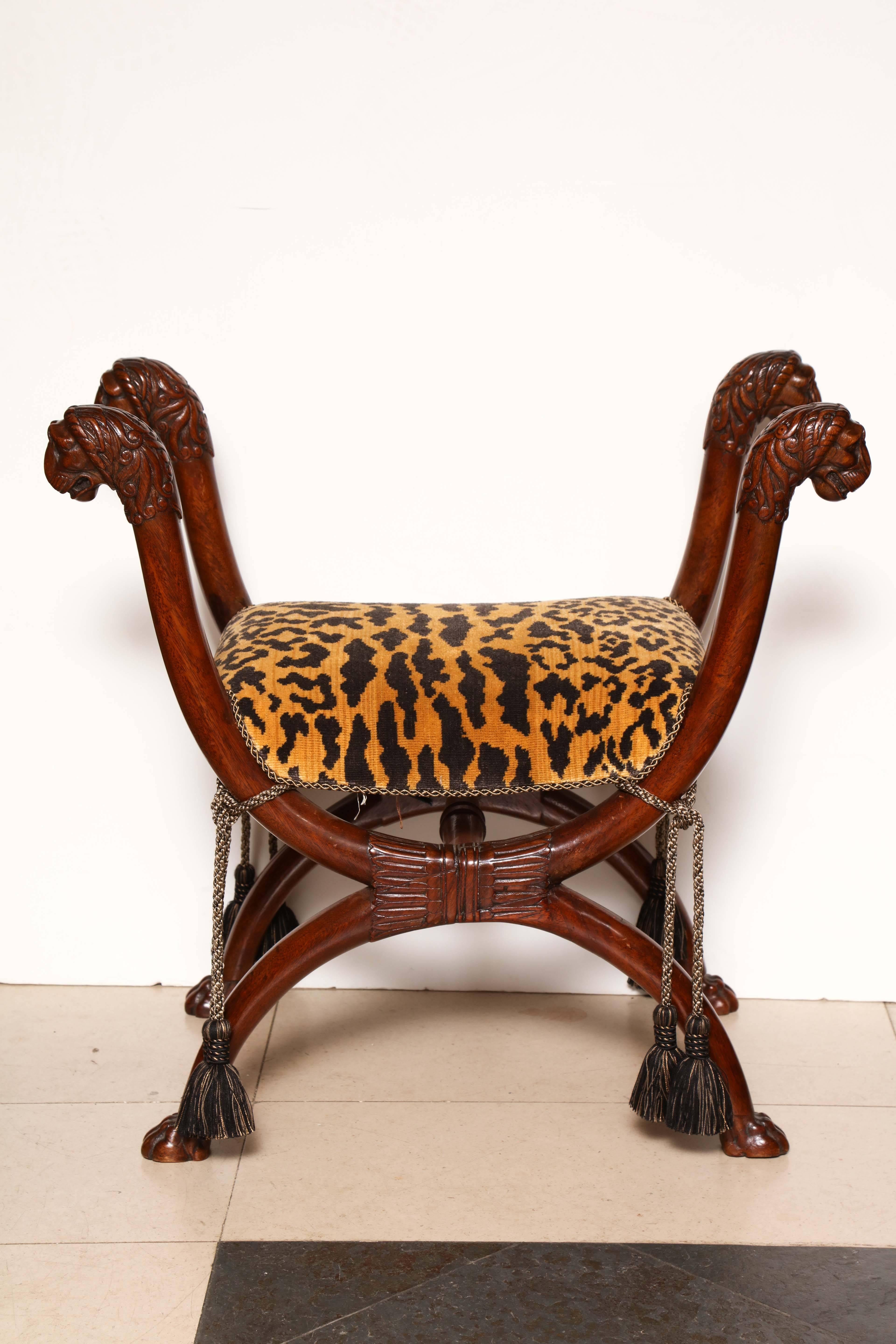 A fine Regency lion head-carved Curule form mahogany stool with carved paw feet.