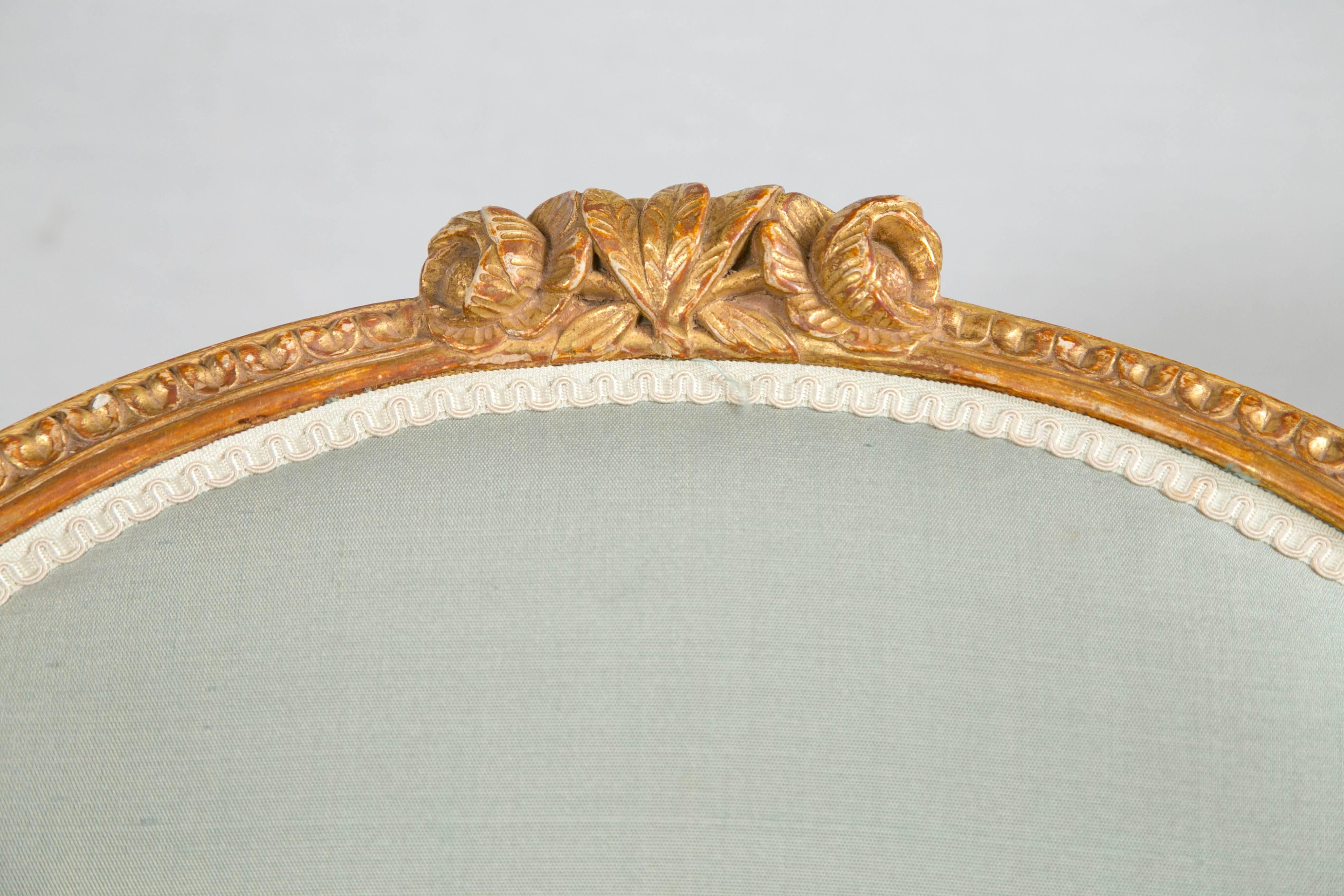 A superb pair of George III carved hand gilded armchairs using 23-carat gold-leaf . Acanthus leaf crest sits atop oval padded seat back. Padded armrests with down-swept supports terminating in a scrolled roundel above turned tapering legs.