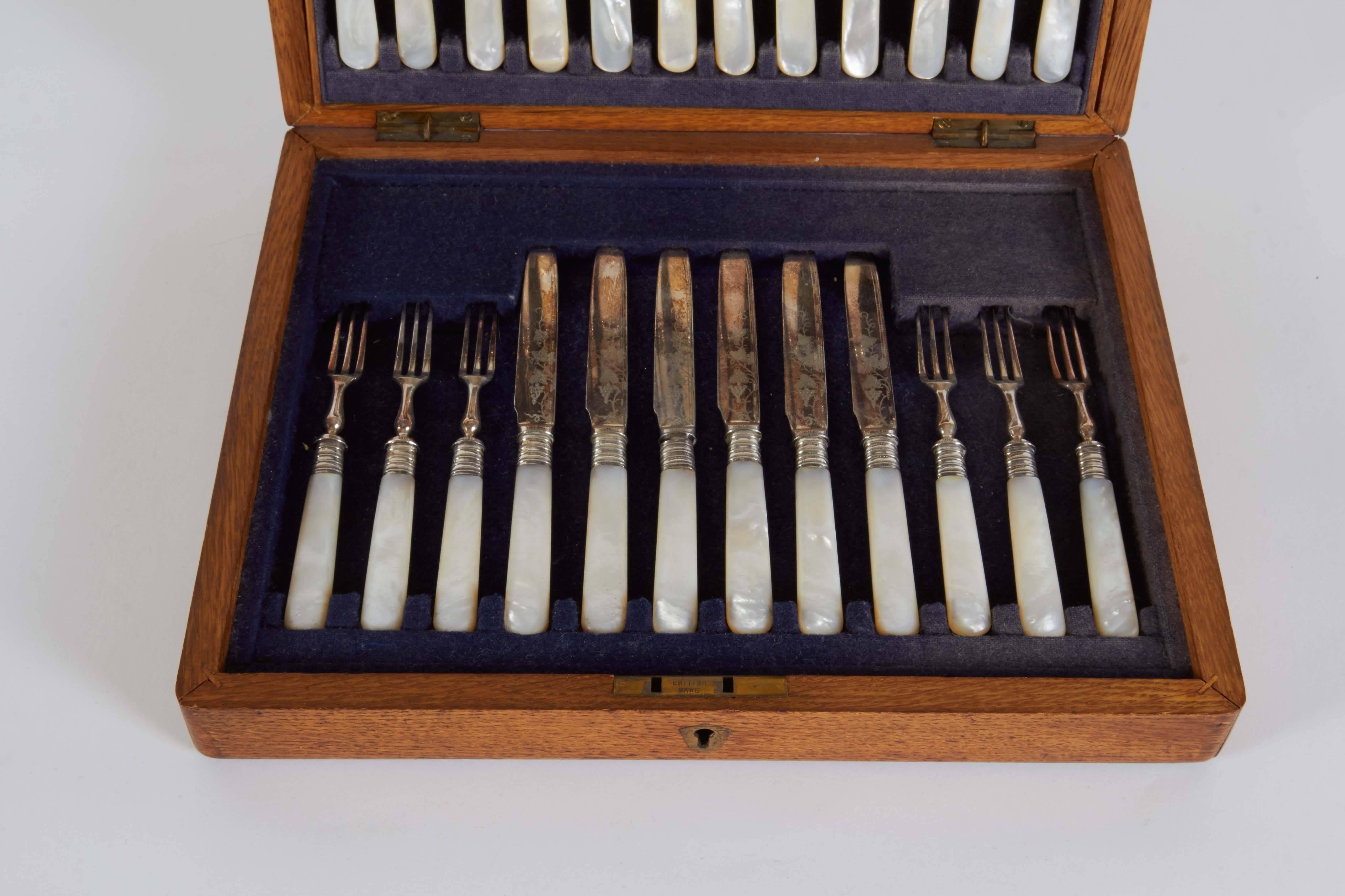 An elegant box set of antique engraved silver plate serve ware comprised of 24 pieces, 12 forks and 12 knives with mother-of-pearl handles.