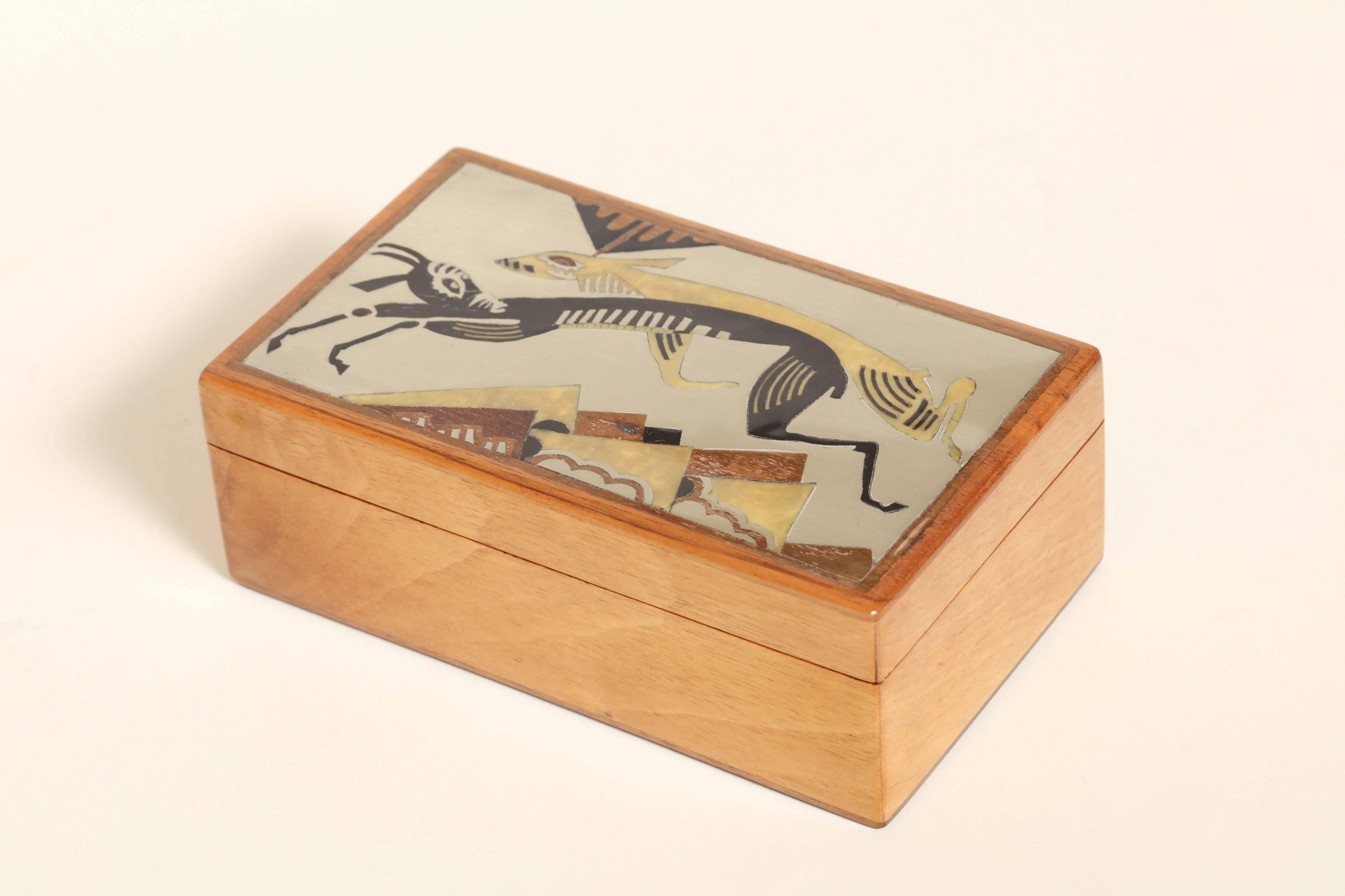Small fruitwood hinged box decorated with antelope leaping above stylized vegetation on the cover in black and cream lacquer and marqueterie wood and metal. 
Apocryphal signature J. Dunand on inside of lid. 
This box is in good condition. The top