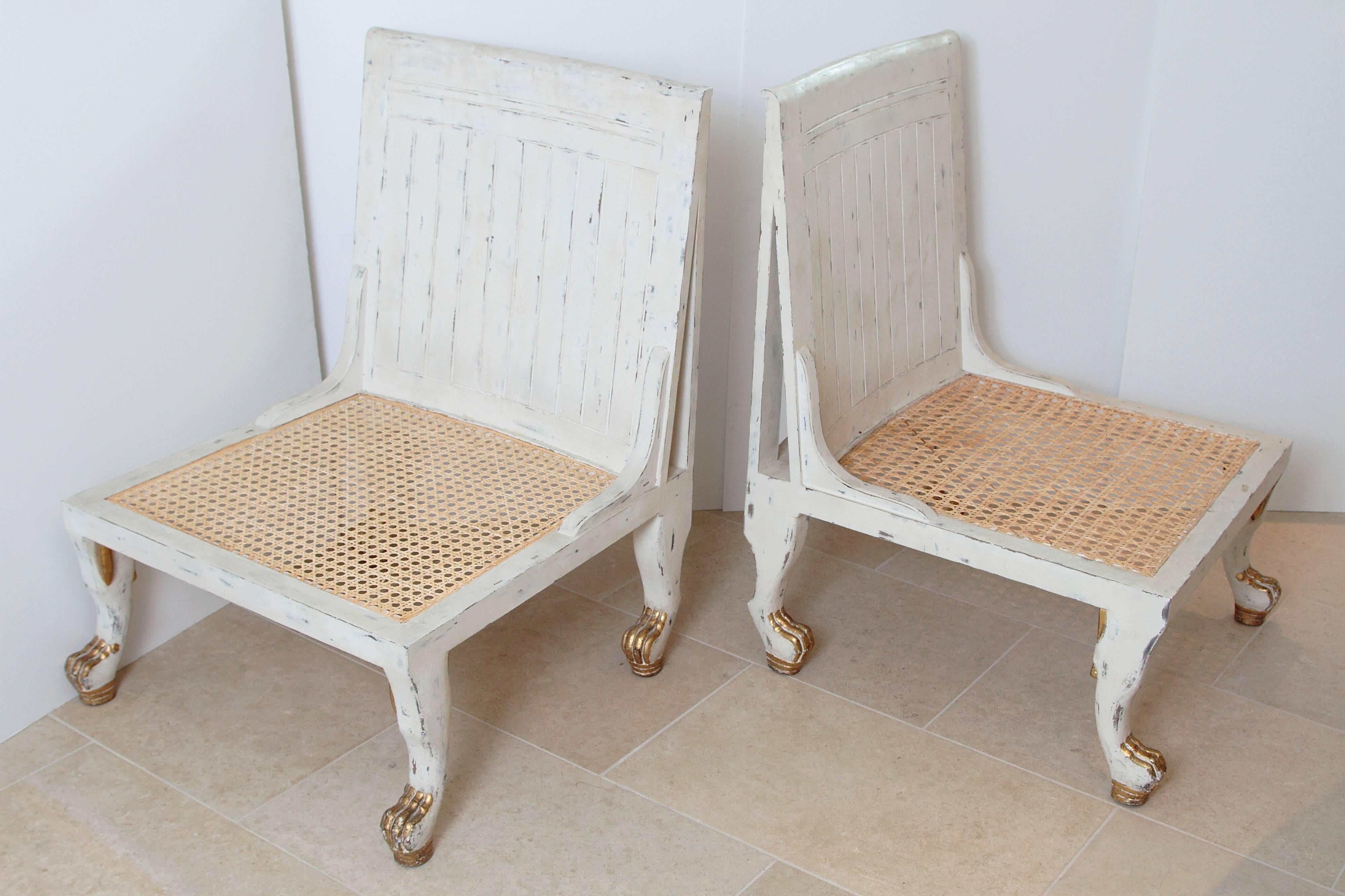In the Egyptian taste, a pair of white painted and parcel-gilt Thebes chairs.

Resting on carved paw feet with caned seats.

Late 20th century.

An absolutely beautiful pair!