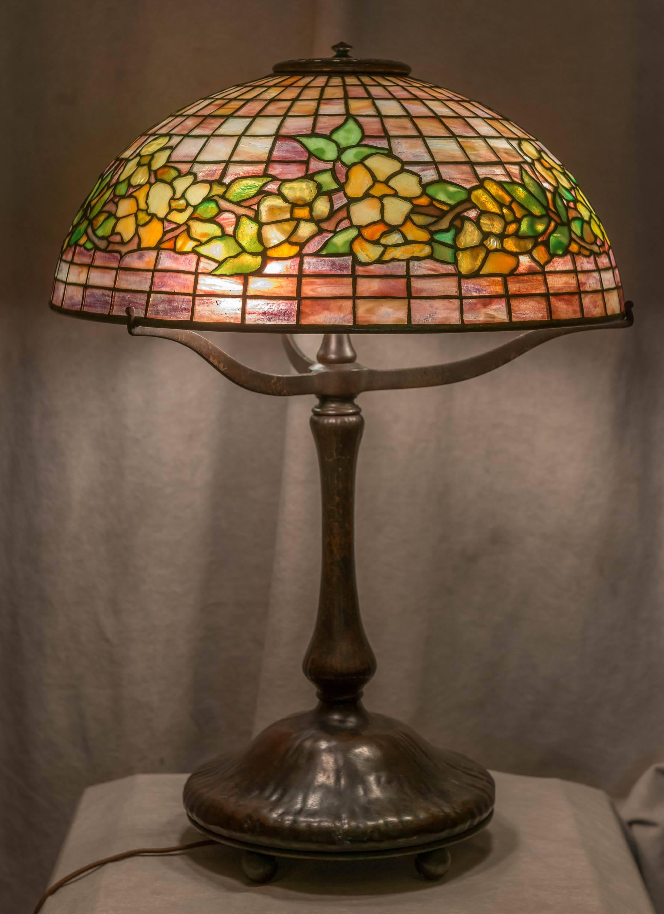 A very nice example of the beauty of the workmanship created by Tiffany Studios. The light lavender or pink background make for a nice contrast with floral design. Mounted on a richly patinated bronze base together make for a desirable package. Base