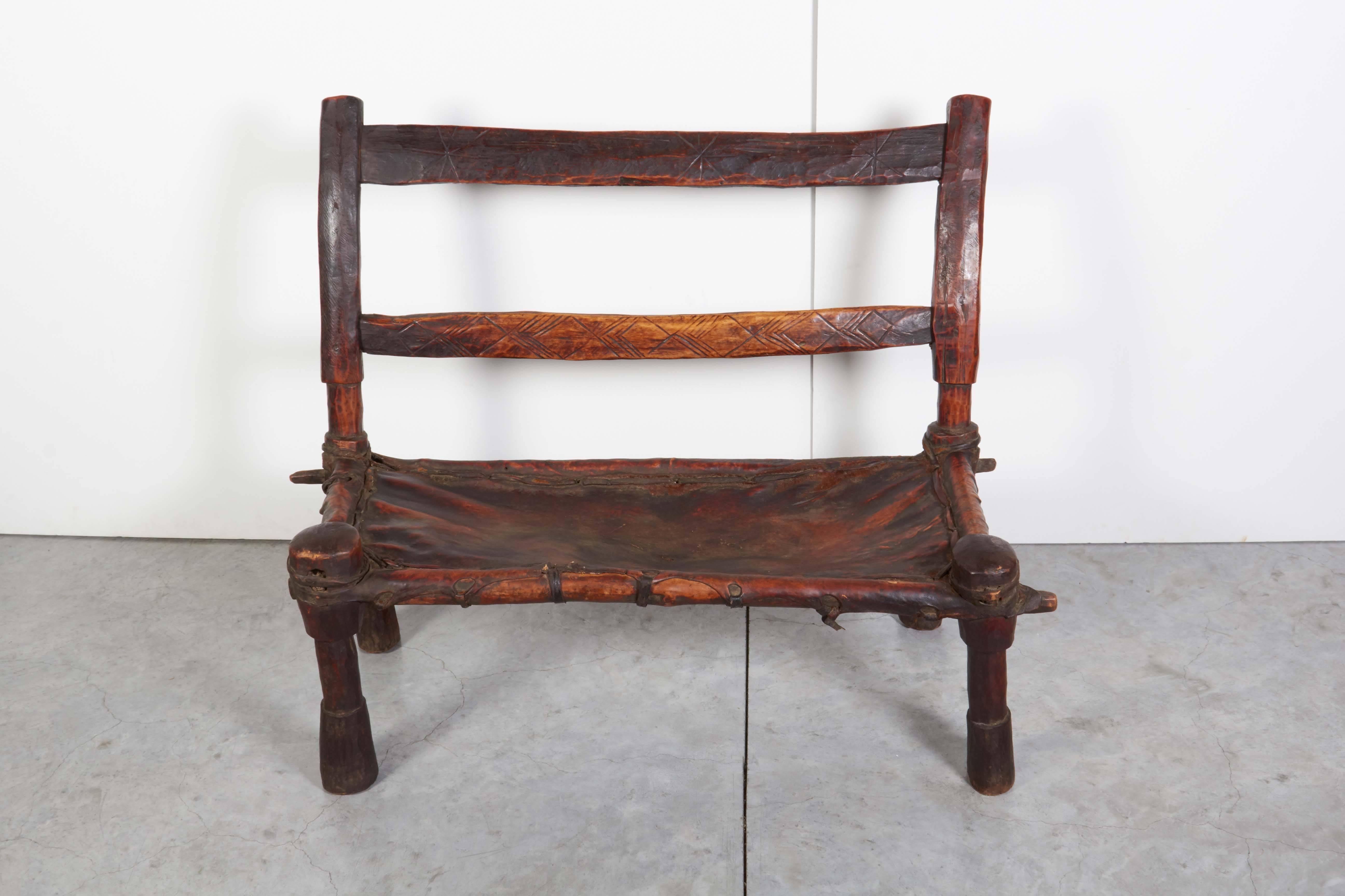 Eine schlichte, rustikale Holzbank mit einem schön abgenutzten Ledersitz und klarem Design. Dieser doppelte Stuhl/Bank aus Äthiopien sieht aus jedem Blickwinkel gut aus und hat eine große Präsenz. 
CH371.