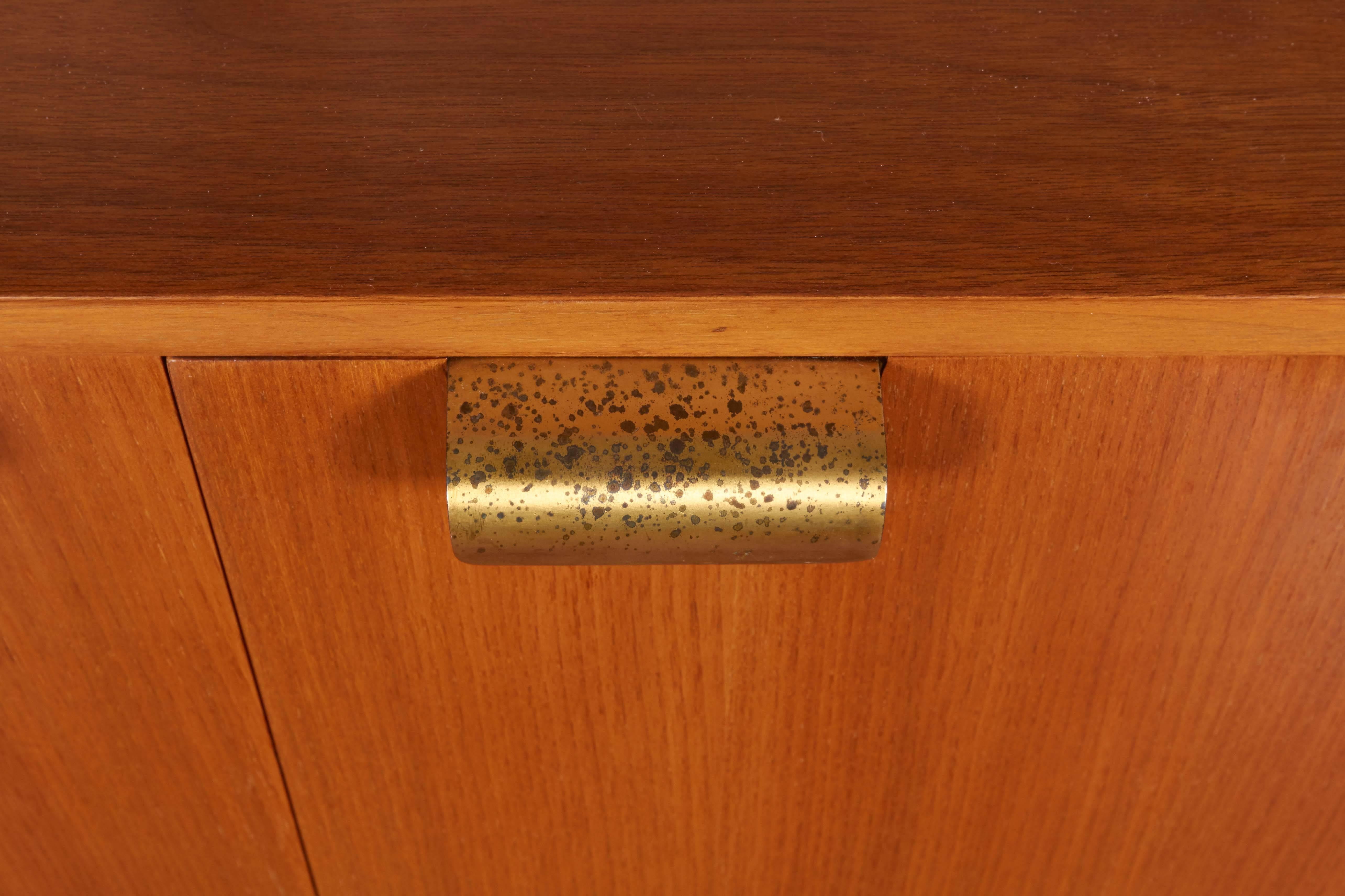 A walnut cabinet by designer George Nelson, manufactured by Herman Miller, circa 1960s. Including two doors, each with brass pull handle, the interior with two shelves of varied tones and grains. Very good vintage condition, wear, including patina