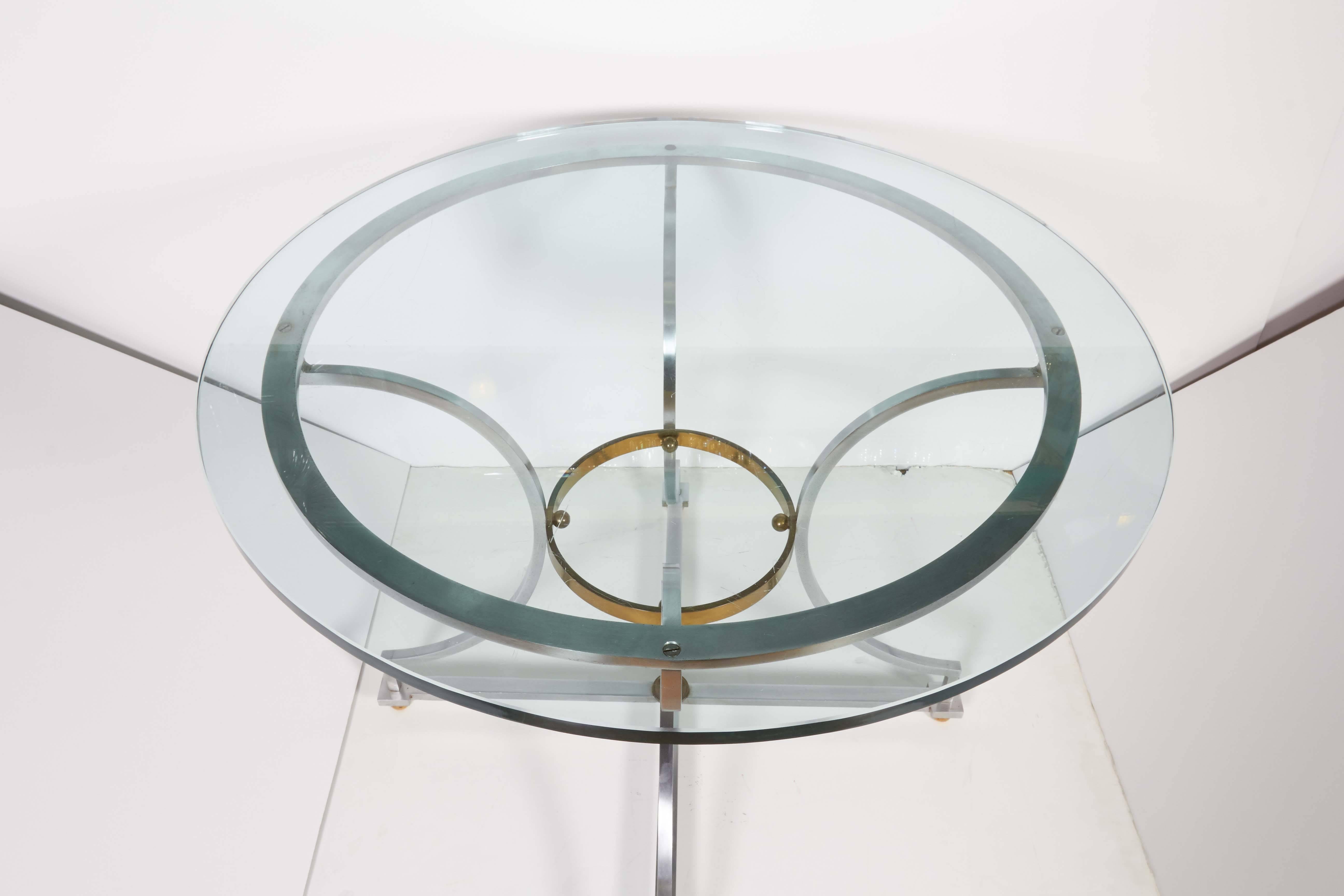 A vintage occasional table, designed in the manner of Maison Jansen, round glass on linear base comprised of brushed steel with brass accents. Measuring glass 3/4